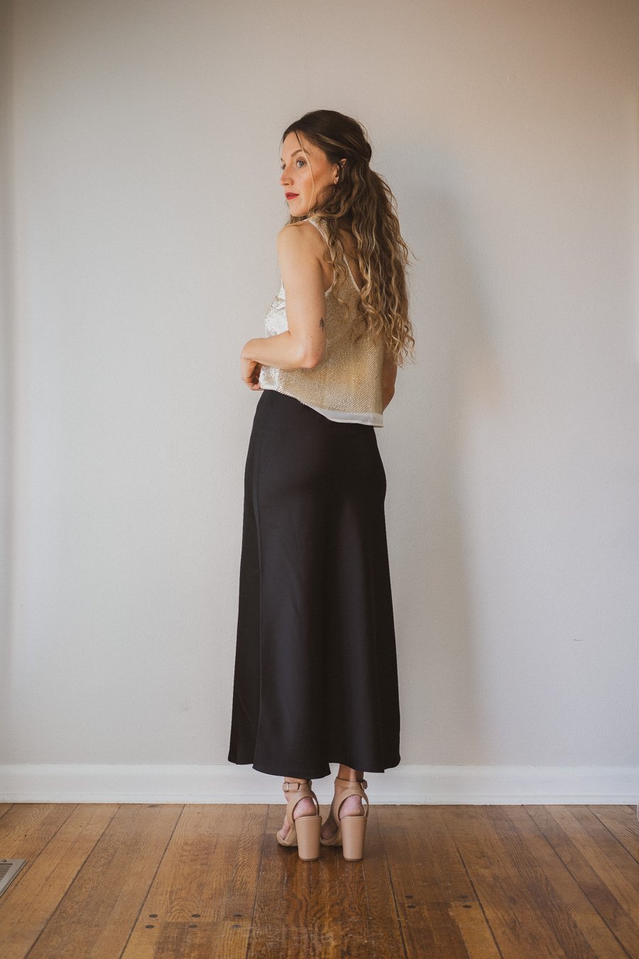 holiday look with a gold sequined top, black midi skirt, tan strappy heels, and a tan leather bag