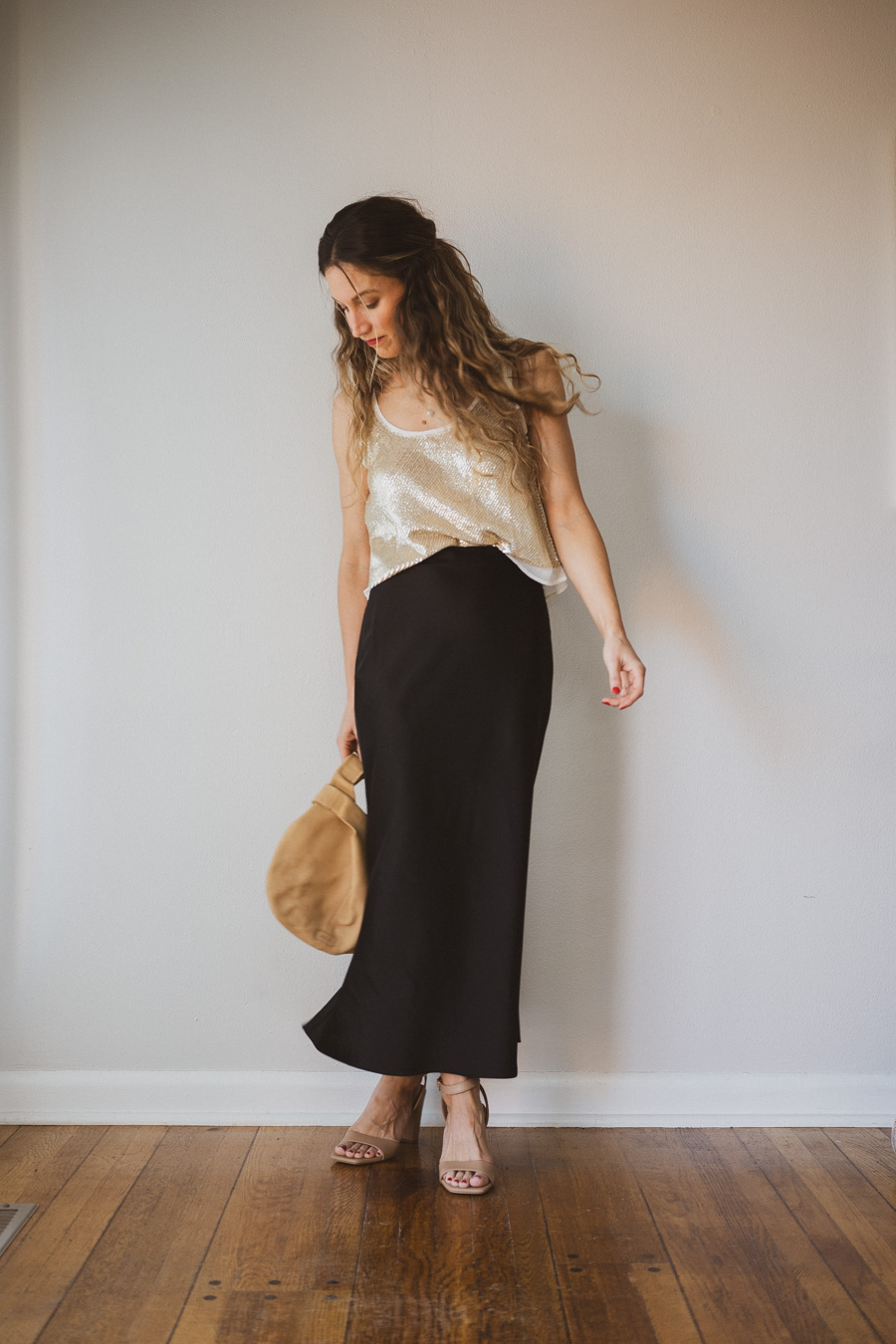 holiday look with a gold sequined top, black midi skirt, tan strappy heels, and a tan leather clutch