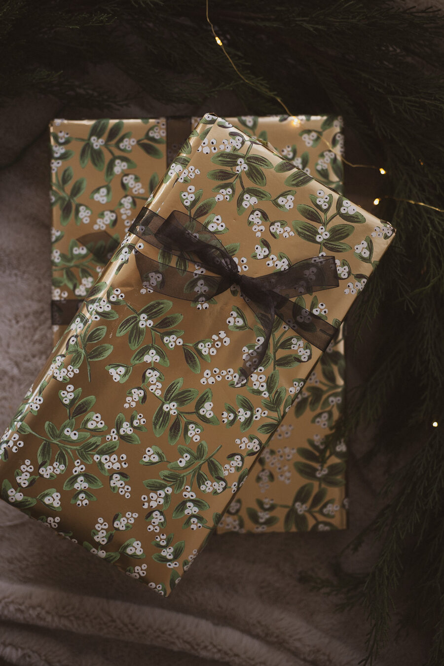 two presents wrapped in gold foil wrapping paper with white and green flowers and black ribbon