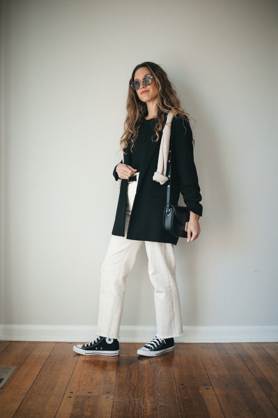 a spring transitional outfit with a black tee, black blazer, ecru straight denim, black high top Converse, and a black crossbody bag