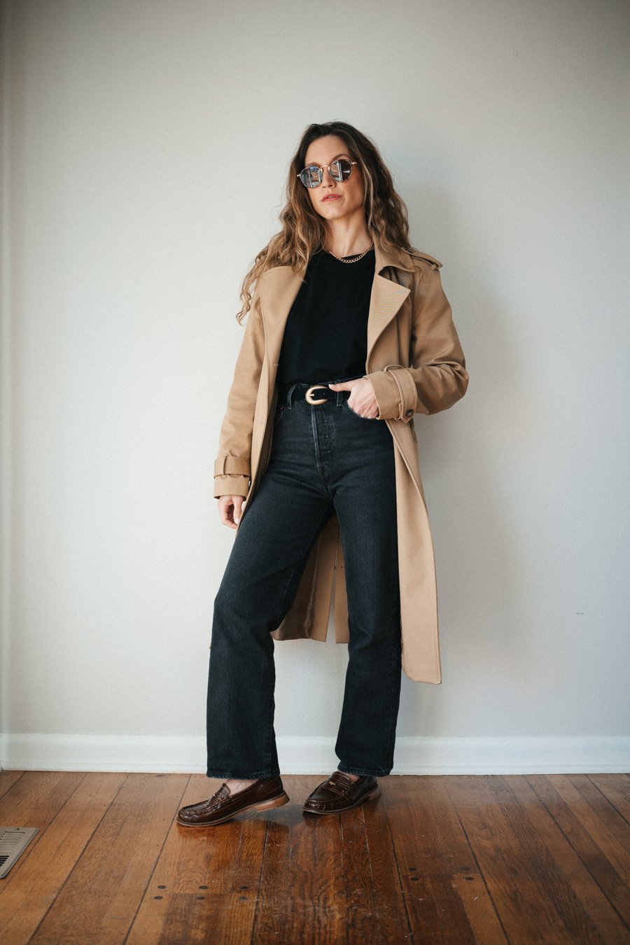 ashley wearing a black tee, black straight denim, tan trench coat, brown loafers, and a black belt