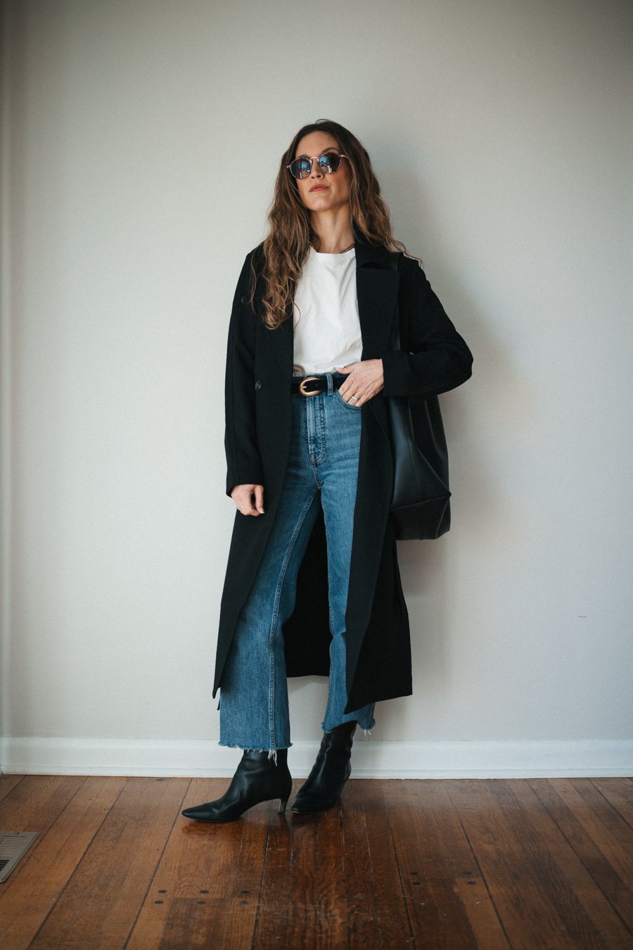 ashley wearing a white tee, black trench coat, medium wash straight cropped jeans, black heeled ankle boots, and a black tote bag