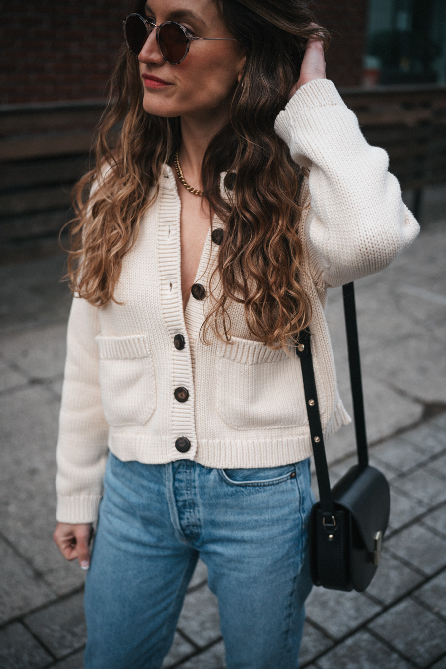 ashley wearing a mom-friendly outfit with a beige cardigan, light wash slim straight jeans, black fisherman sandals, and a black crossbody bag