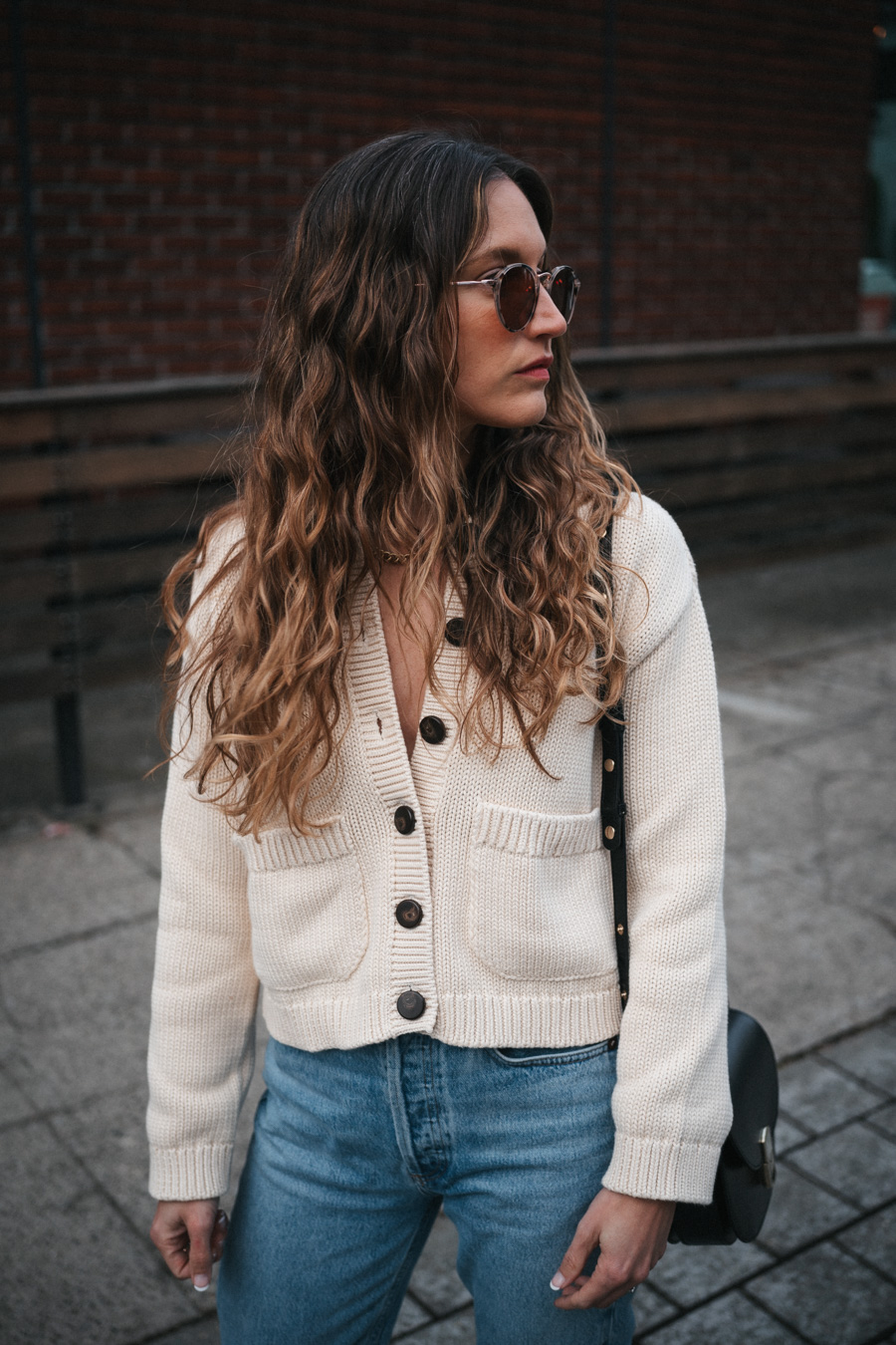 ashley wearing a mom-friendly outfit with a beige cardigan, light wash slim straight jeans, black fisherman sandals, and a black crossbody bag