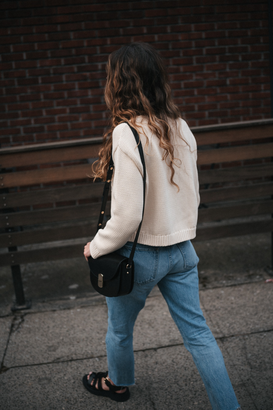 ashley wearing a mom-friendly outfit with a beige cardigan, light wash slim straight jeans, black fisherman sandals, and a black crossbody bag