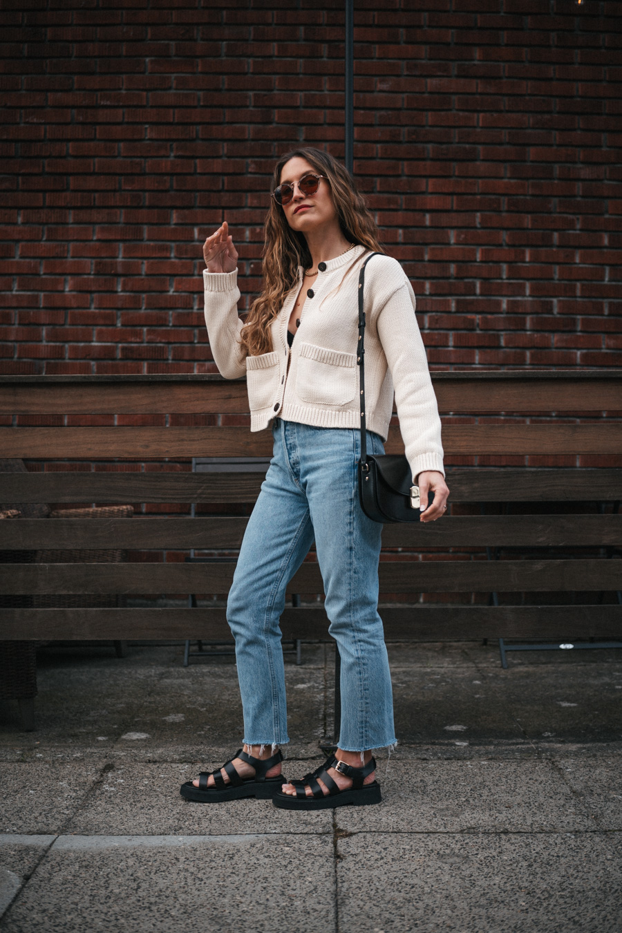 ashley wearing a mom-friendly outfit with a beige cardigan, light wash slim straight jeans, black fisherman sandals, and a black crossbody bag