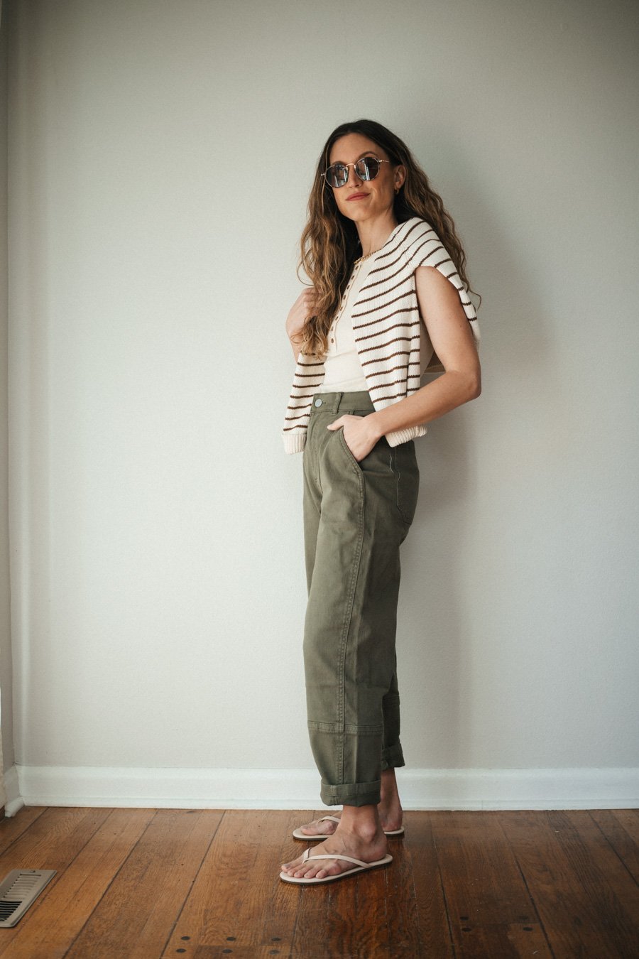 outfit with green cargo pants, ecru henley tank, a striped camel and ecru sweater worn over the shoulders, and ivory sandals