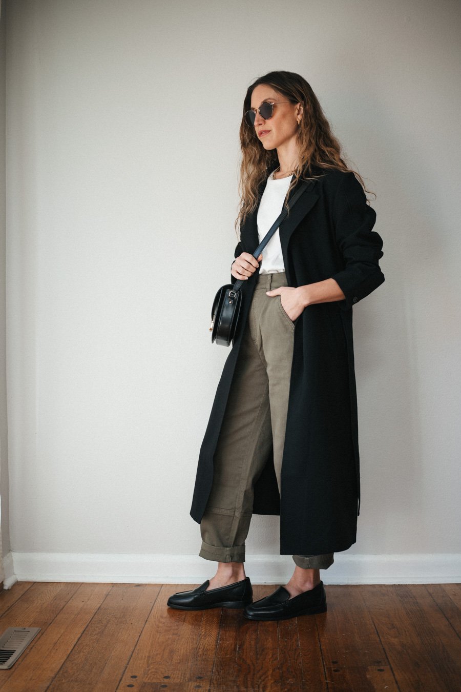 outfit with green pants, white tee, black trench, black loafers, and a black crossbody bag