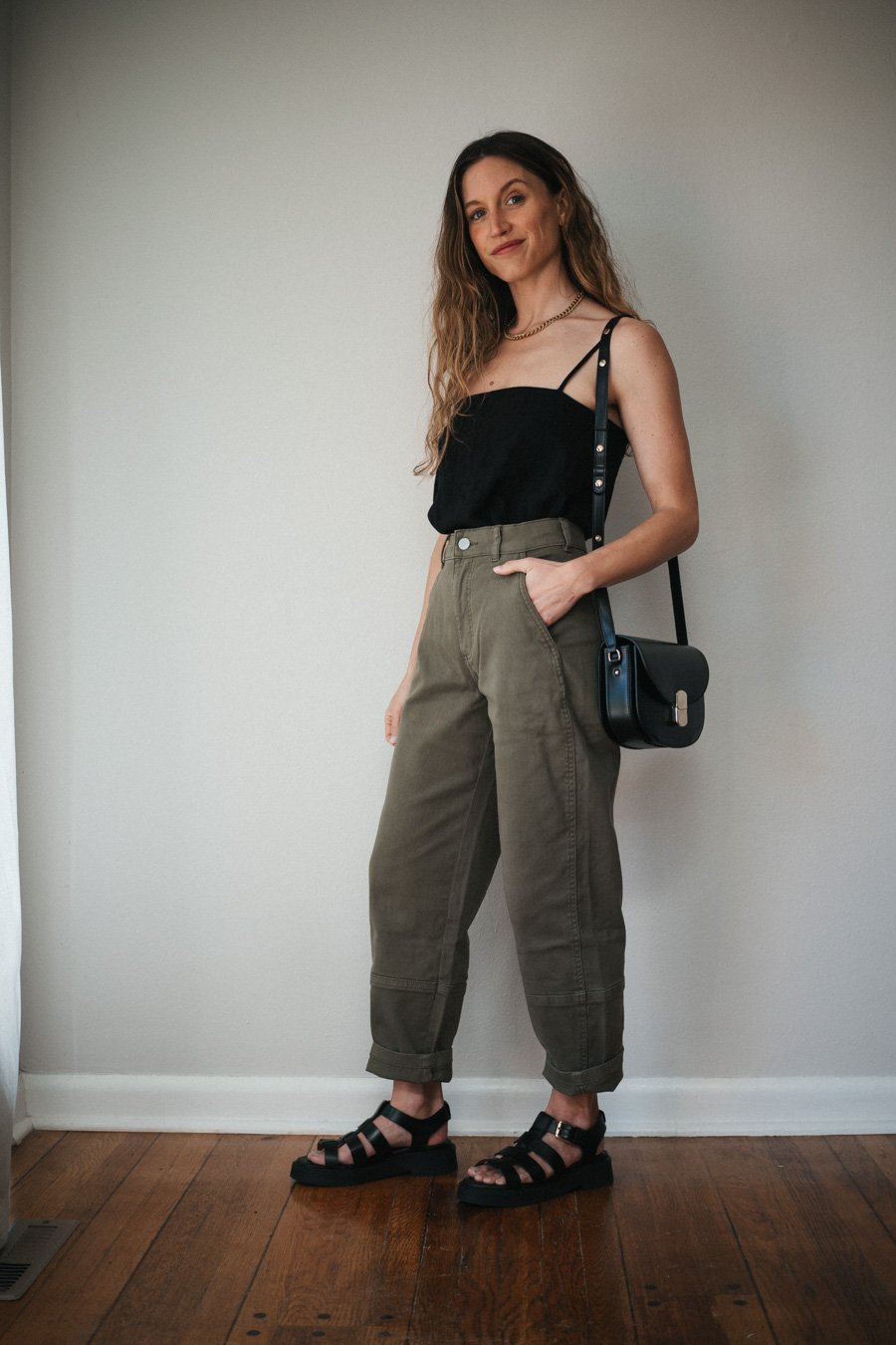 spring outfit with green pants, a black tank, and black fisherman sandals, and a black crossbody bag