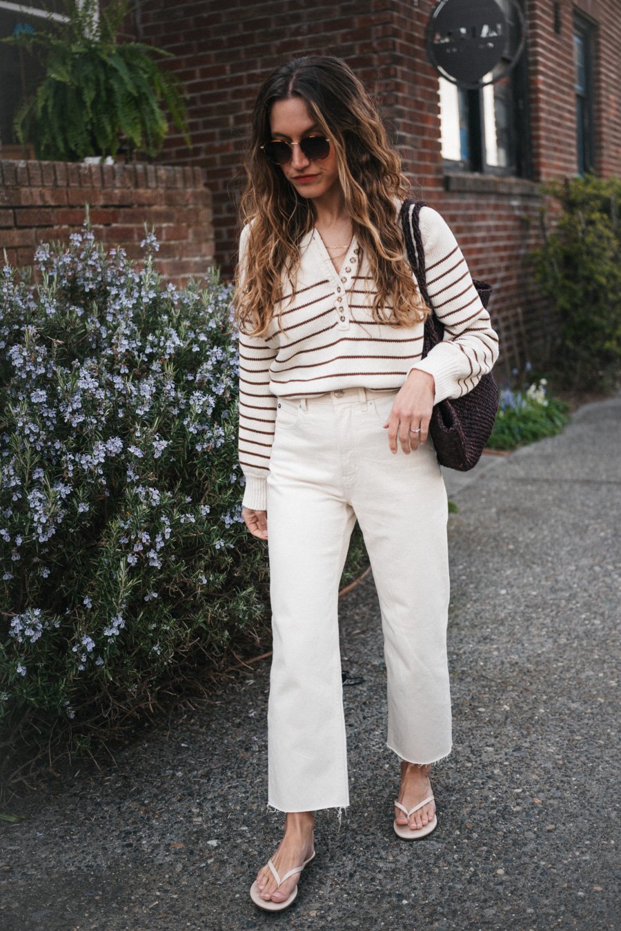 ashley wearing the Sézane Léontine Jumper with white denim, ivory sandals, and a brown woven tote bag