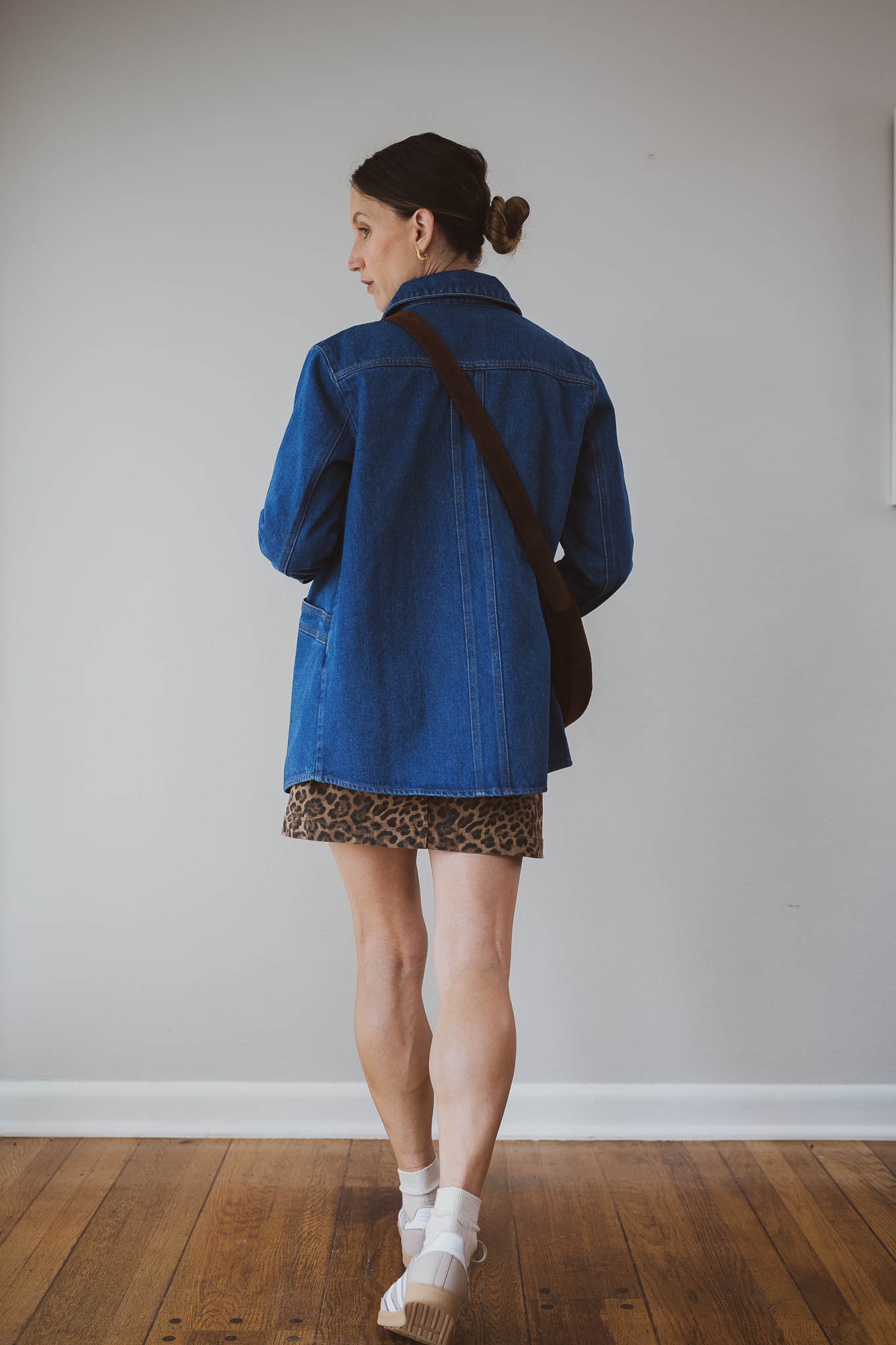 fall outfit idea with a beige knit sweater, leopard print mini skirt, dark wash denim jacket, Adidas Samba sneakers, and socks