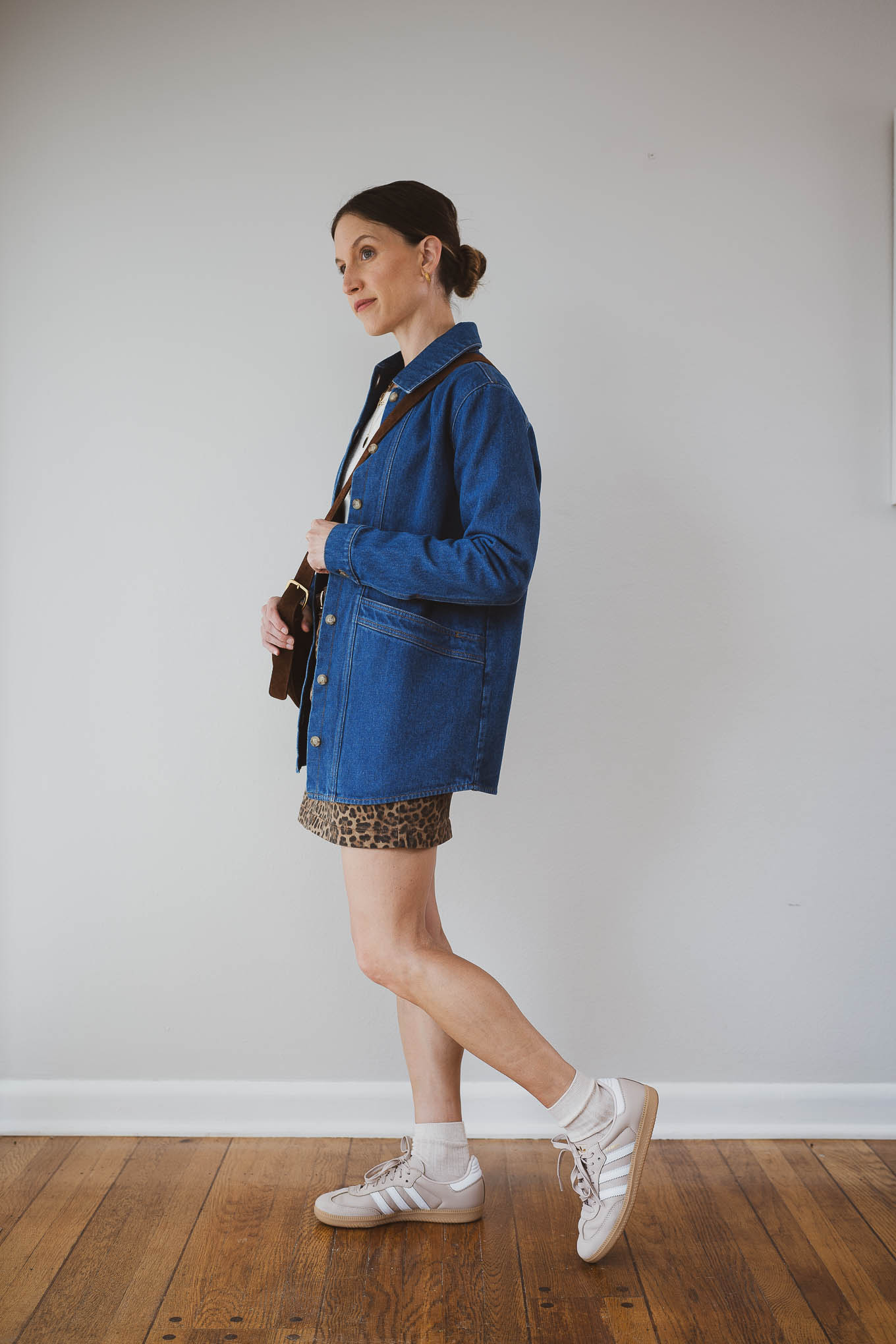 fall outfit idea with a beige knit sweater, leopard print mini skirt, dark wash denim jacket, Adidas Samba sneakers, and socks