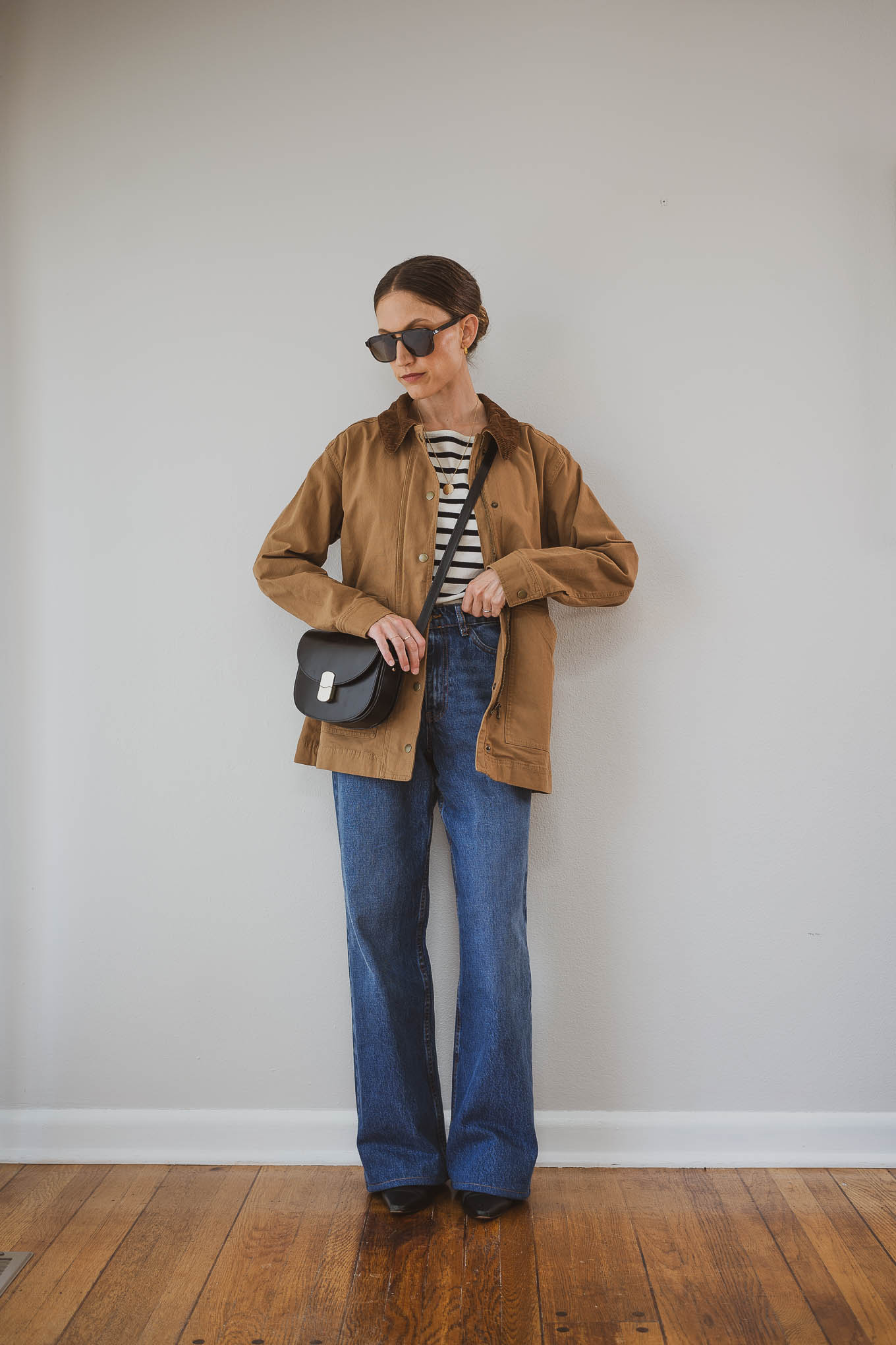 fall capsule wardrobe outfit with a black and white striped top, barn jacket, medium wash wide leg jeans, and black boots