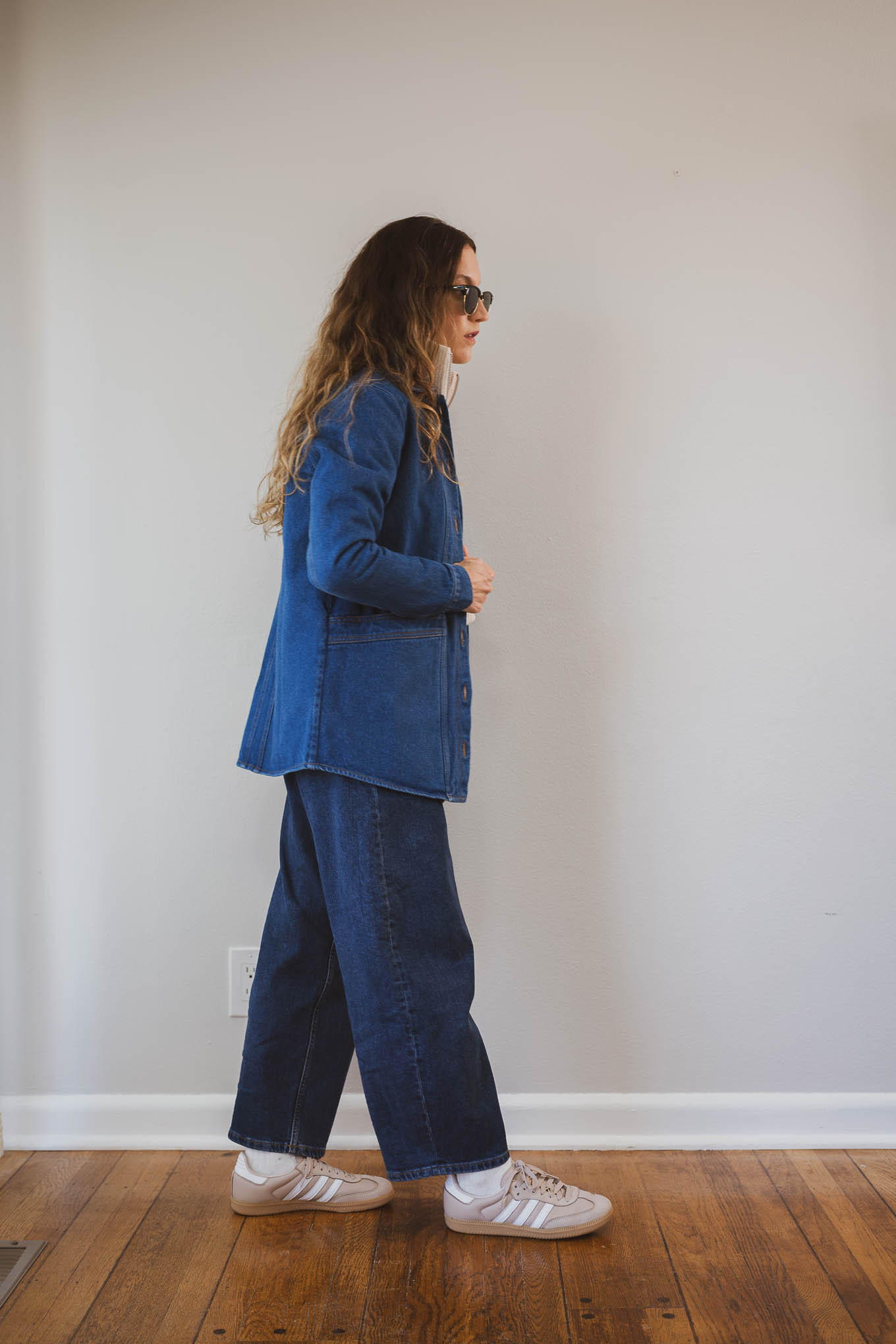 fall capsule wardrobe outfit with a beige half-zip wool sweater, dark wash denim jacket, dark wash barrel jeans, and tan Adidas Samba sneakers