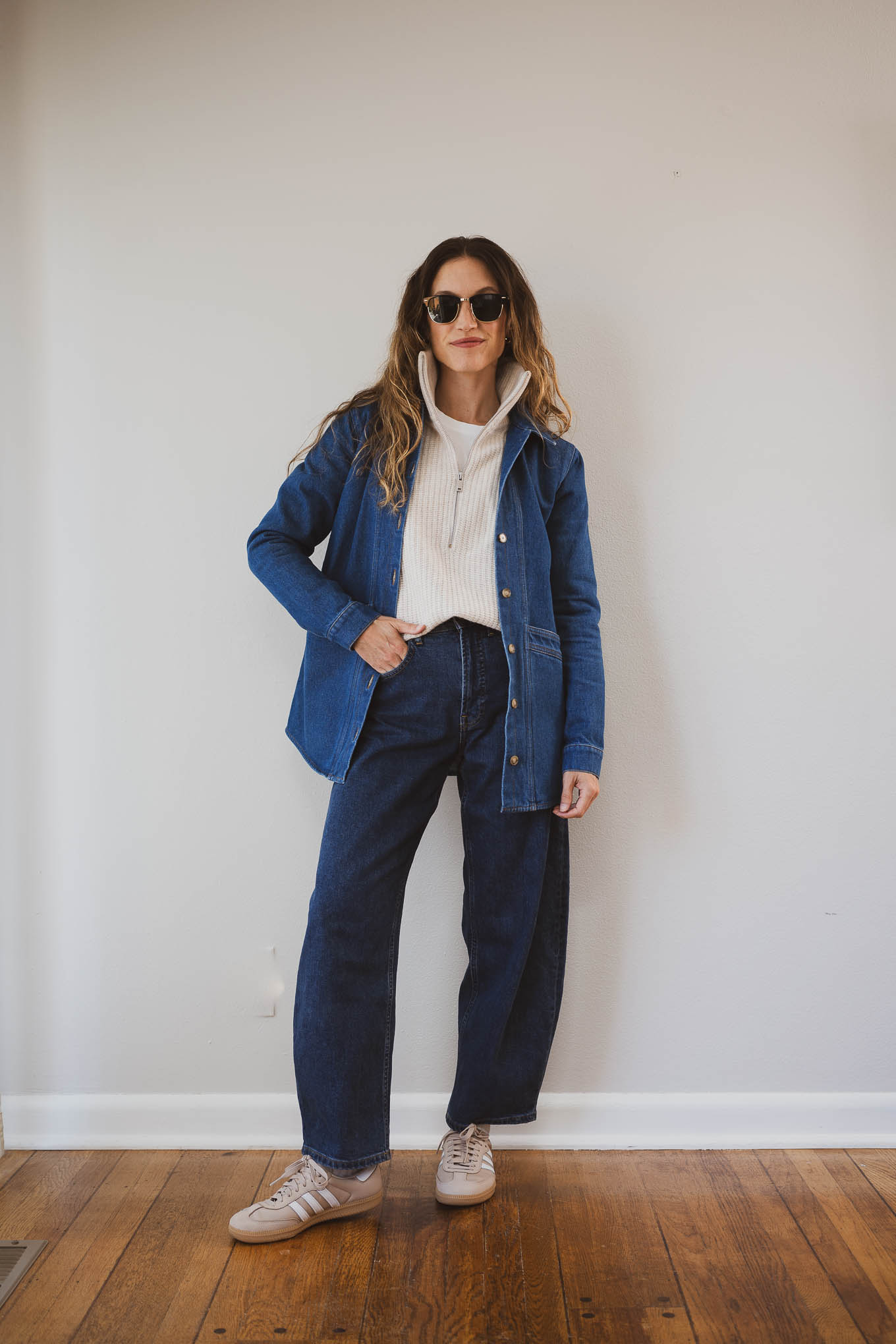 fall capsule wardrobe outfit with a beige half-zip wool sweater, dark wash denim jacket, dark wash barrel jeans, and tan Adidas Samba sneakers