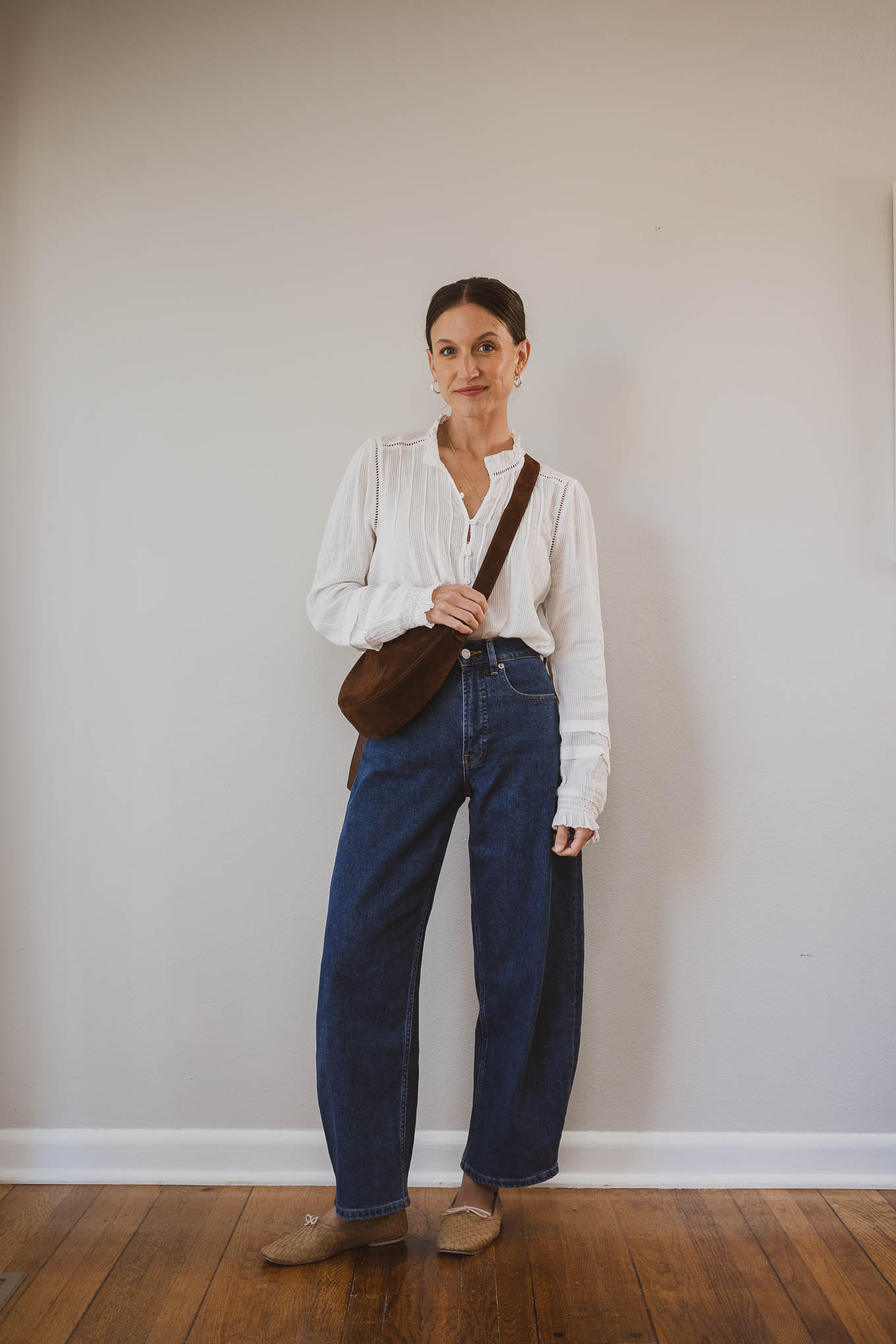 fall capsule wardrobe outfit with a white blouse, barrel jeans, tan woven ballet flats, and a brown suede crossbody bag