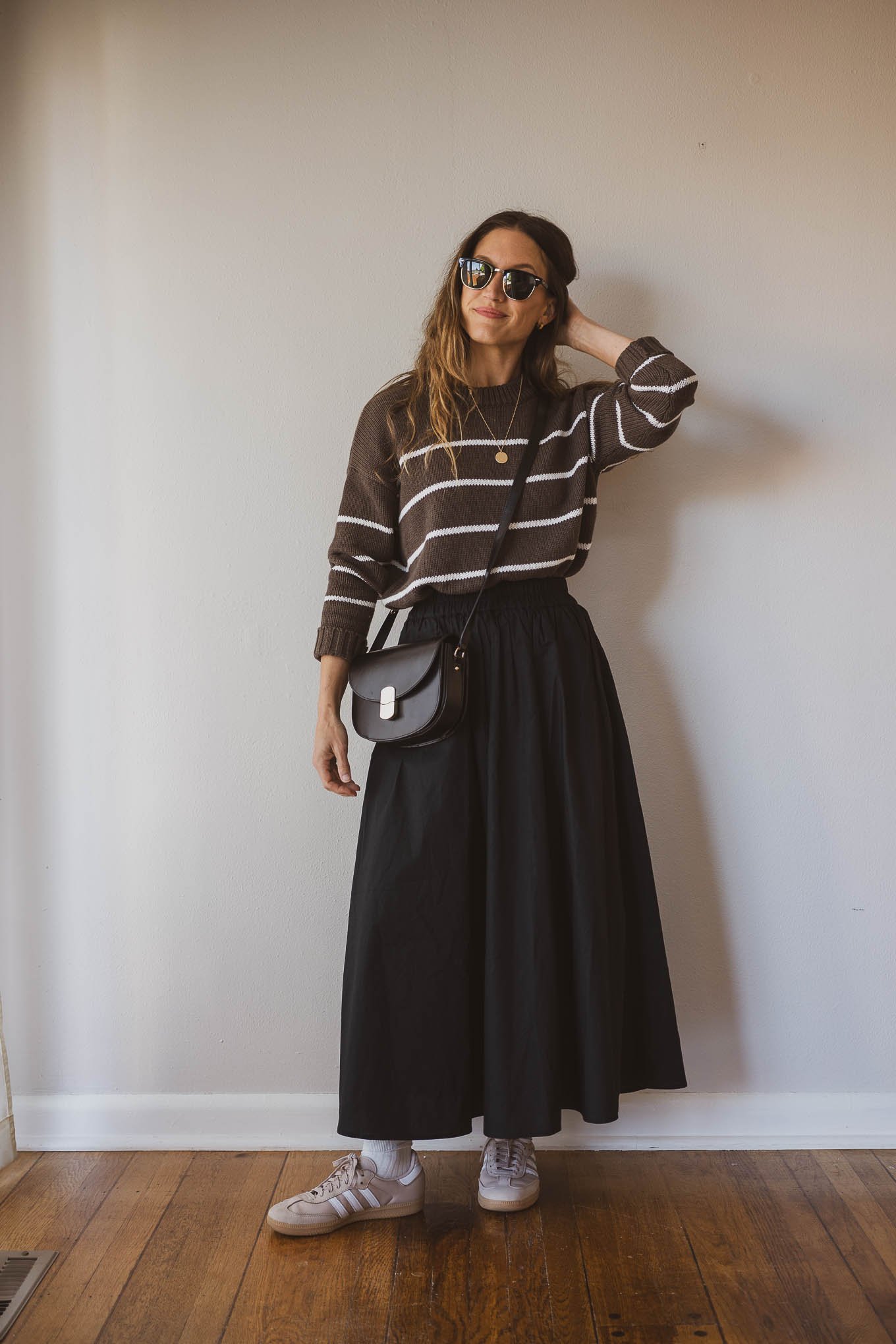 fall outfit idea with a brown and white striped sweater, black full maxi skirt, Adidas Samba sneakers with socks, and a black crossbody bag