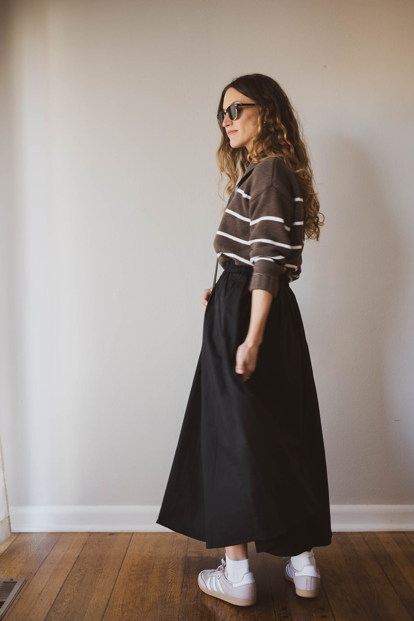 fall outfit idea with a brown and white striped sweater, black full maxi skirt, Adidas Samba sneakers with socks, and a black crossbody bag