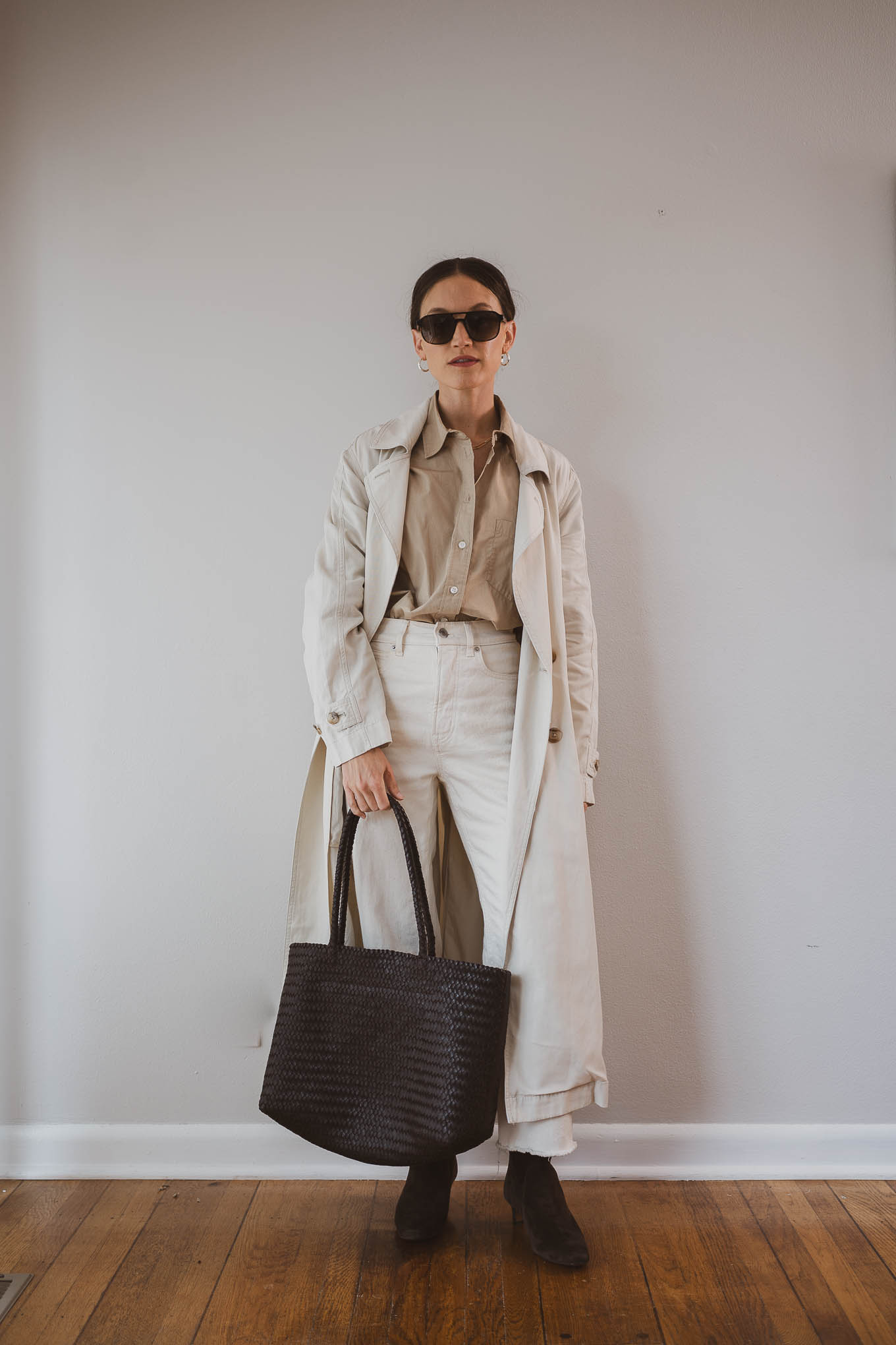 fall capsule wardrobe outfit with a tan button down shirt tucked into ecru straight leg jeans, with a light beige trench coat, brown suede boots, and a brown woven tote bag