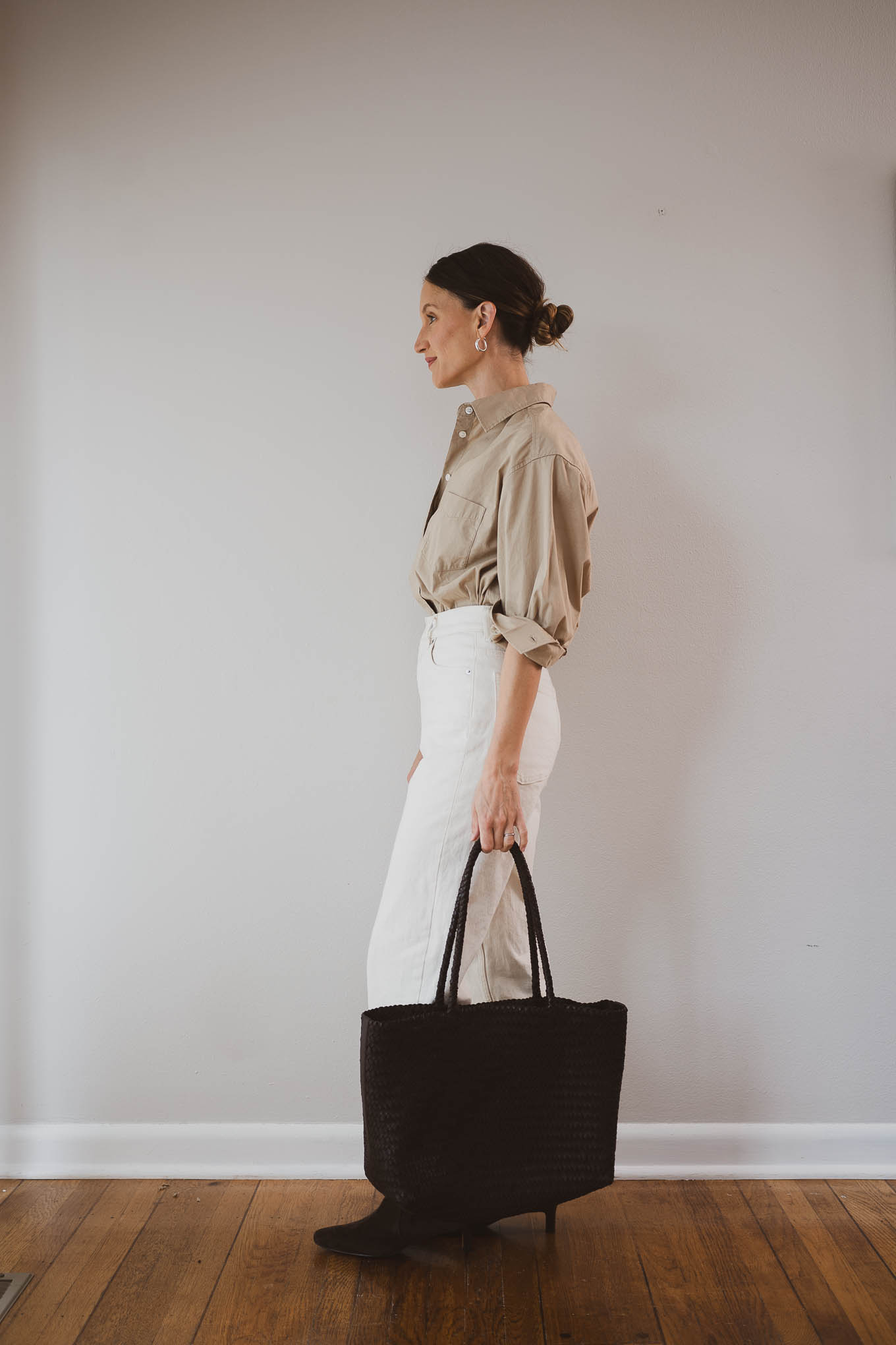 fall capsule wardrobe outfit with a tan button down shirt tucked into ecru straight leg jeans, with a light beige trench coat, brown suede boots, and a brown woven tote bag