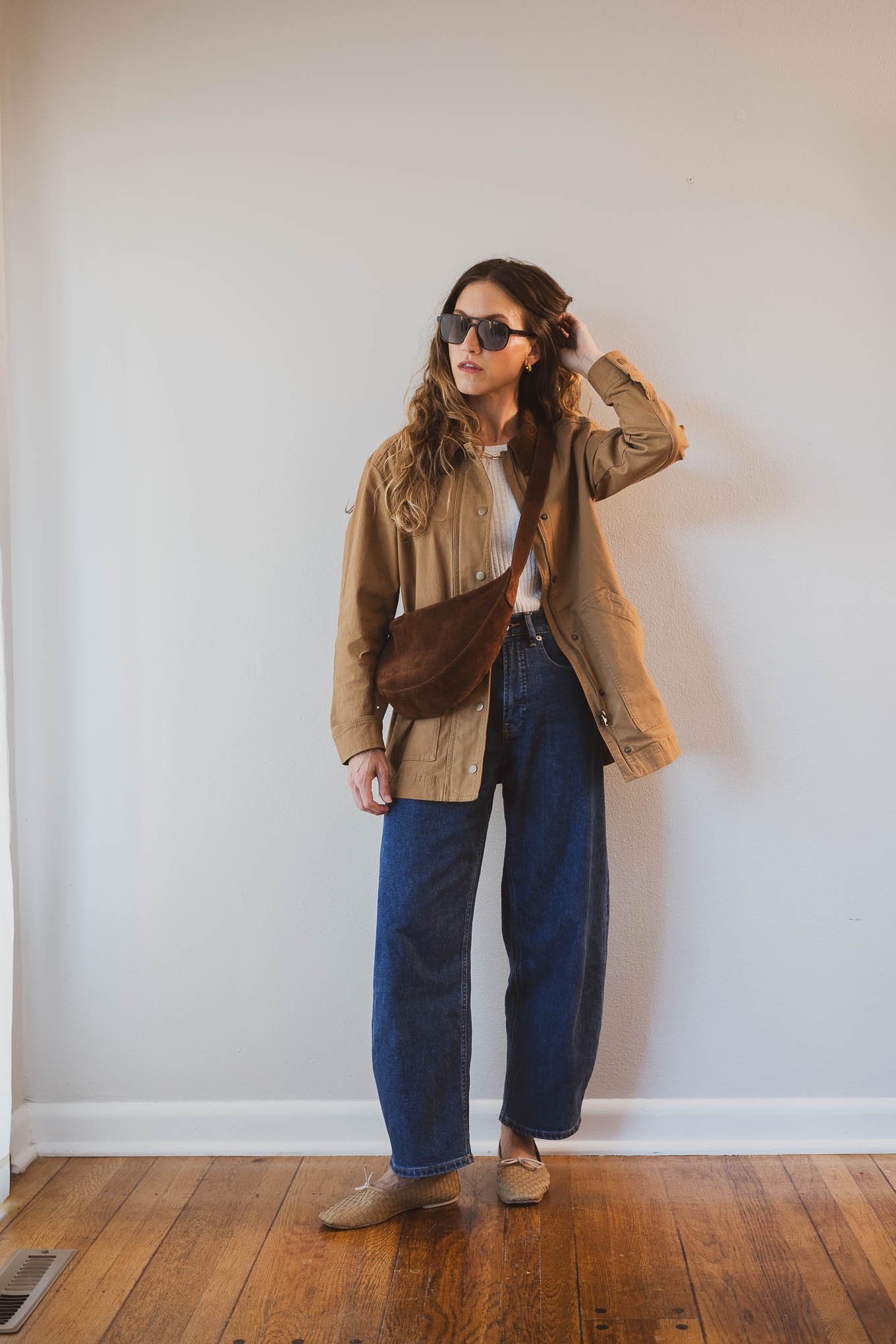 fall capsule wardrobe outfit with a beige fitted sweater, barn jacket, barrel jeans, tan woven ballet flats and a brown suede crossbody bag