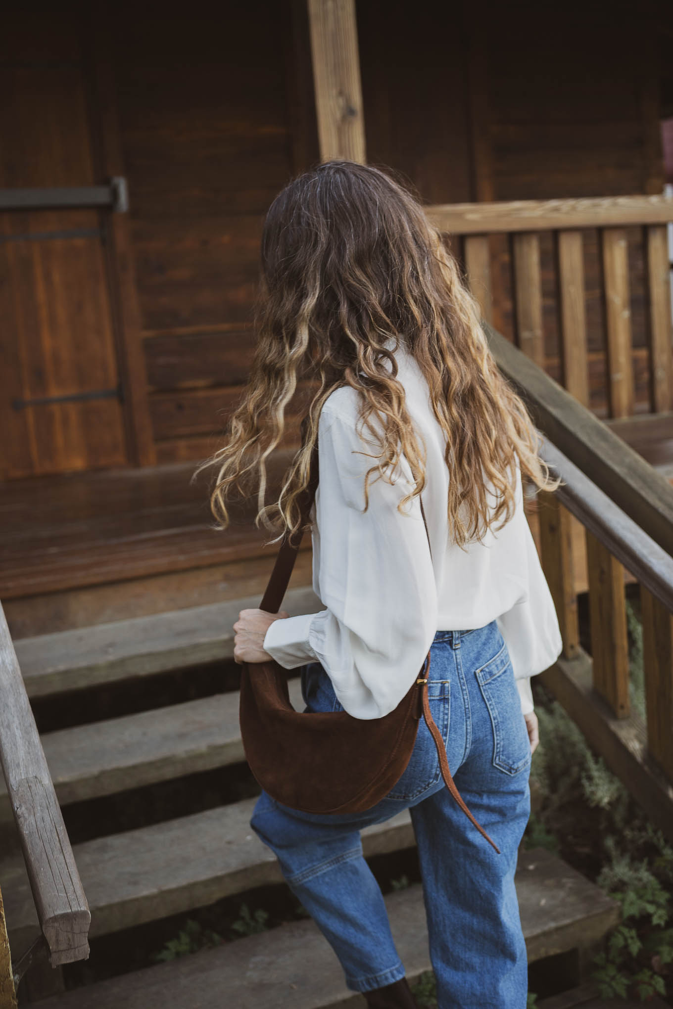 western inspired outfit with a henley silk top, barrel style utility jeans, suede boots, and a suede crossbody bag