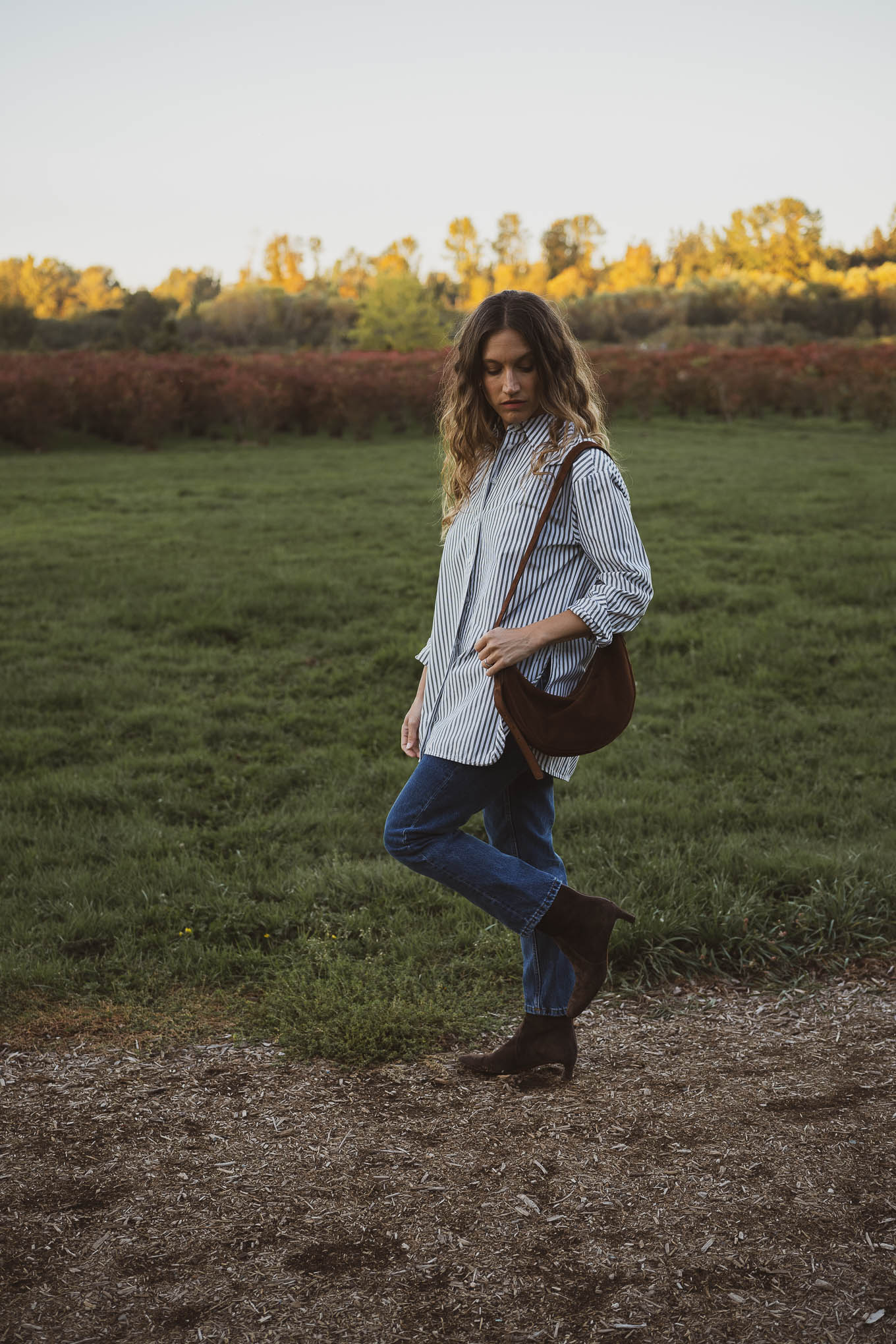 western inspired outfit with an oversized striped button down, slim cut straight leg jeans, brown suede boots, and a brown suede crossbody bag