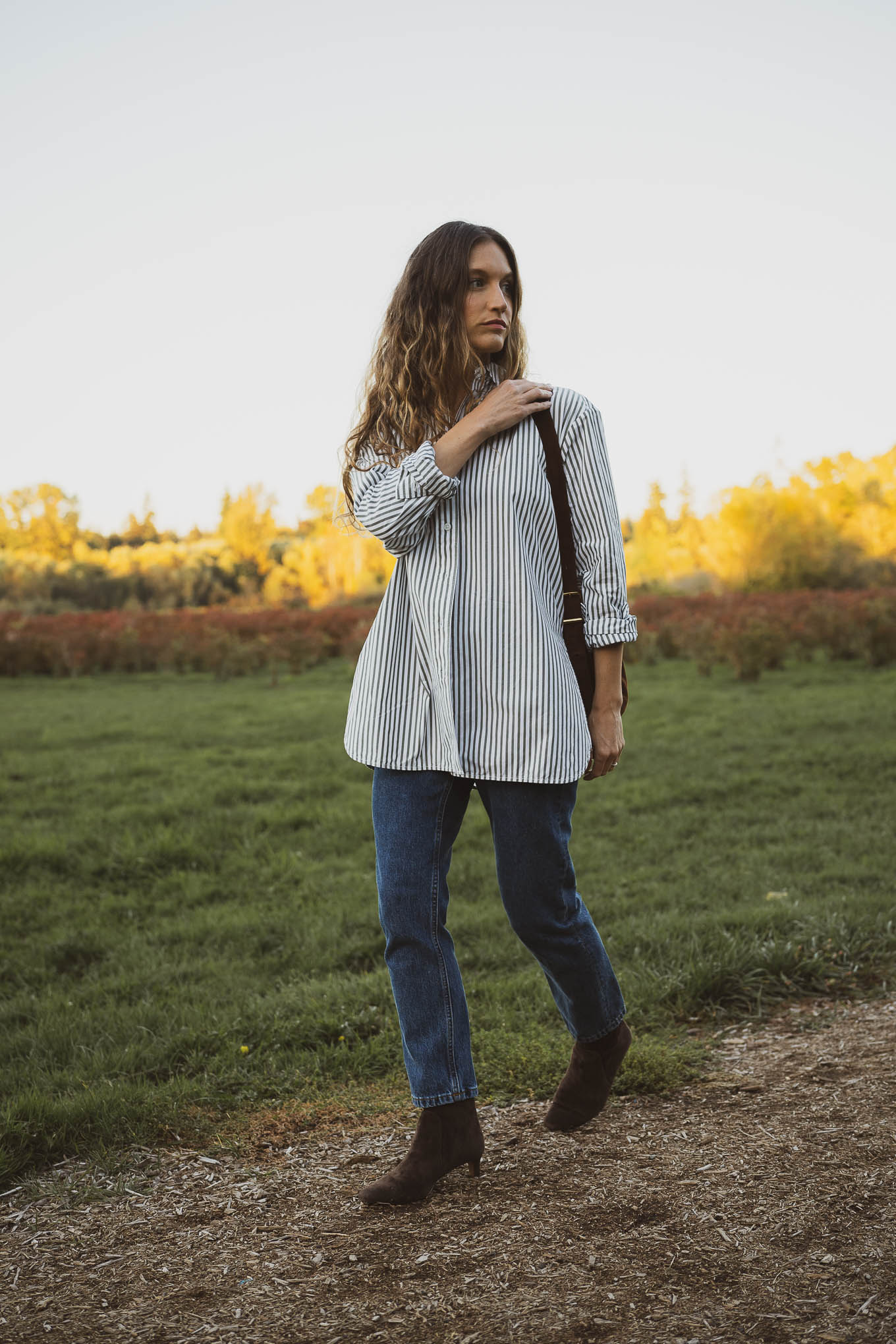 western inspired outfit with an oversized striped button down, slim cut straight leg jeans, brown suede boots, and a brown suede crossbody bag