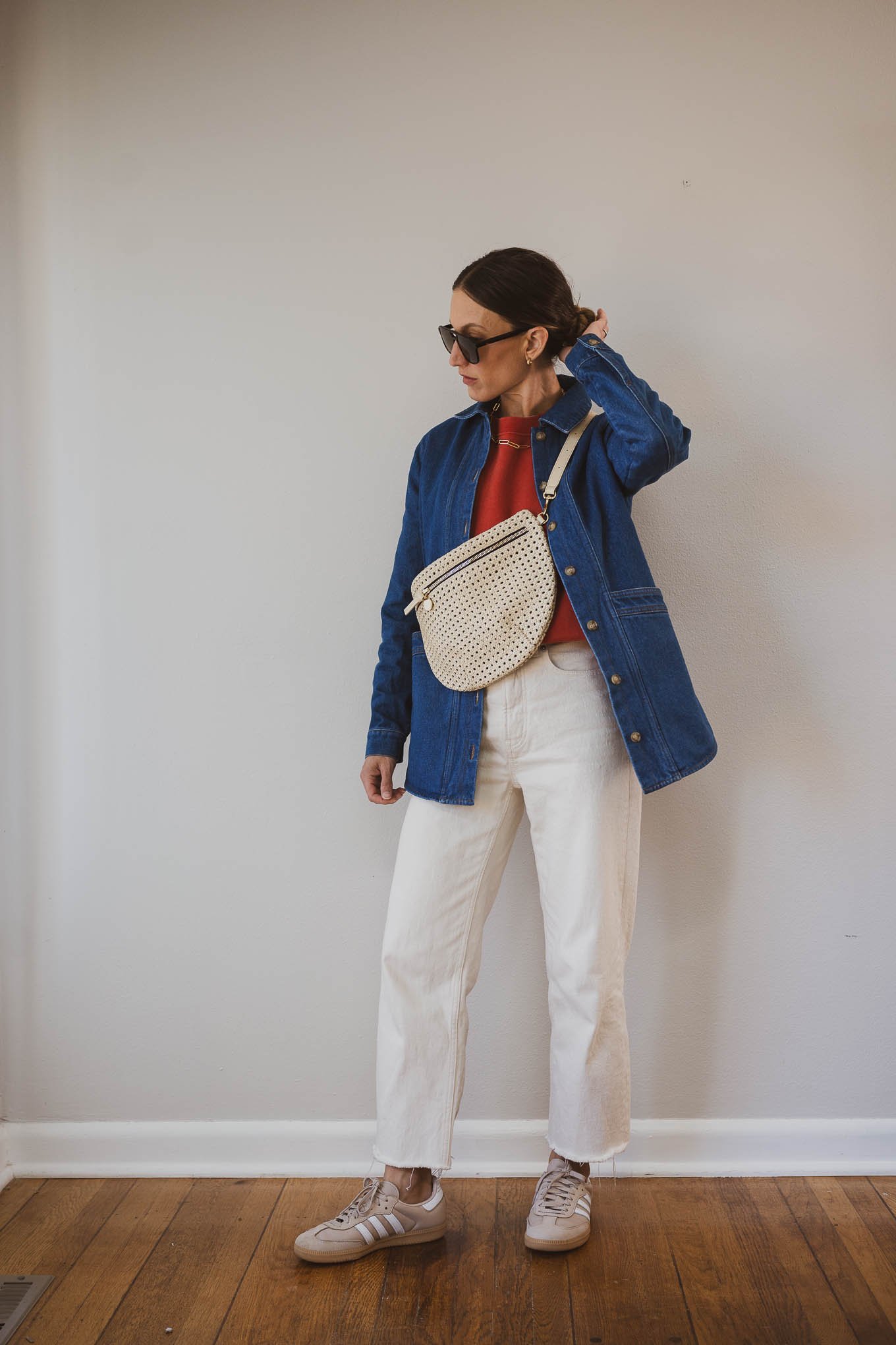 fall capsule wardrobe outfit with a red sweatshirt, denim jacket, ecru jeans, Adidas Samba sneakers, and a cream sling bag