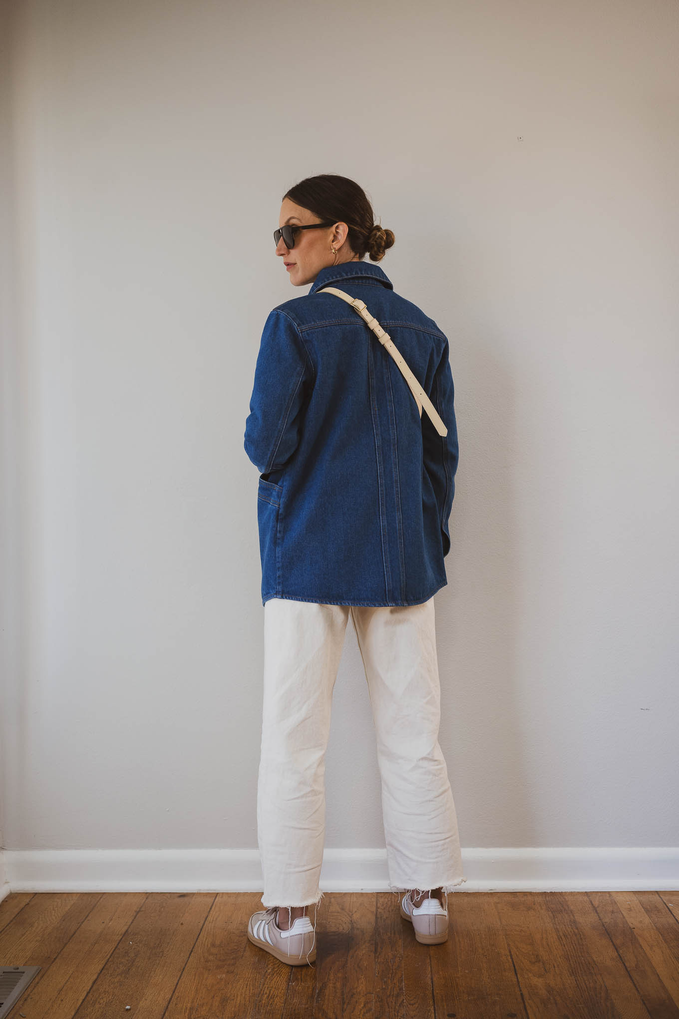 fall capsule wardrobe outfit with a red sweatshirt, denim jacket, ecru jeans, Adidas Samba sneakers, and a cream sling bag
