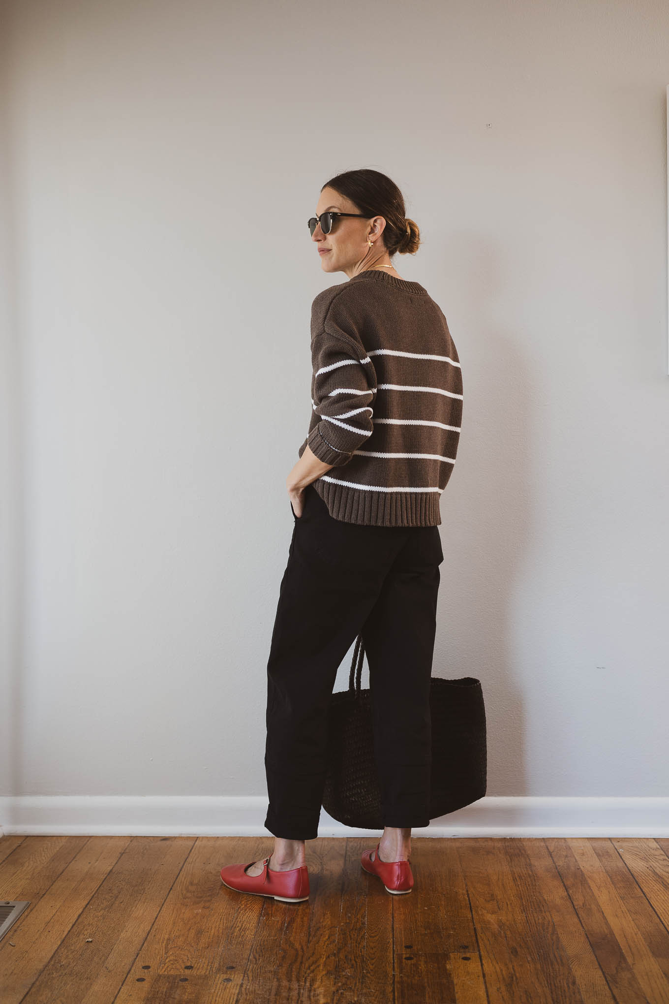 fall outfit idea with a brown and white striped sweater, black barrel leg pants, red Mary Jane ballet flats, and a brown woven tote bag