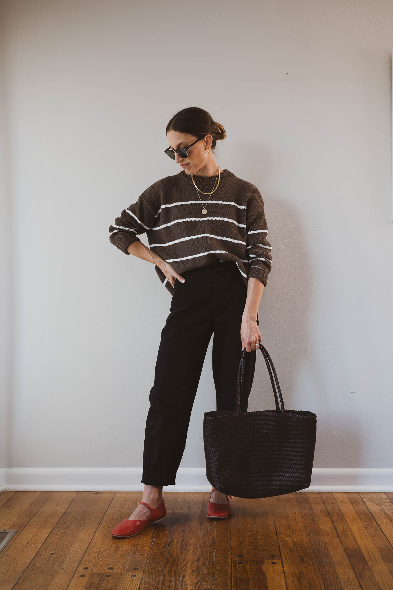 fall outfit idea with a brown and white striped sweater, black barrel leg pants, red Mary Jane ballet flats, and a brown woven tote bag