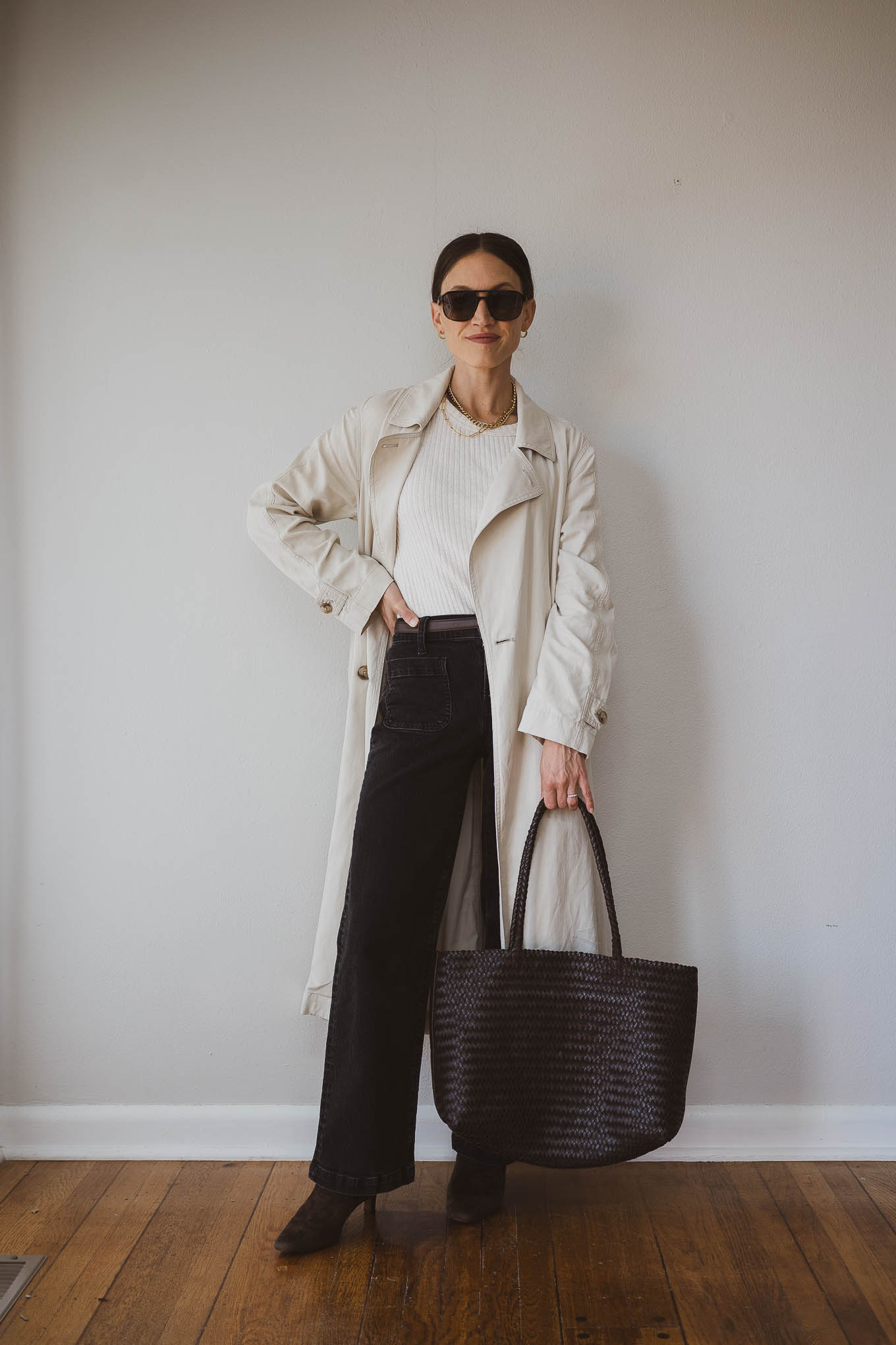 fall capsule wardrobe outfit idea with a beige fitted sweater, beige trench coat, black jeans, brown heeled ankle boots, and a brown woven tote bag