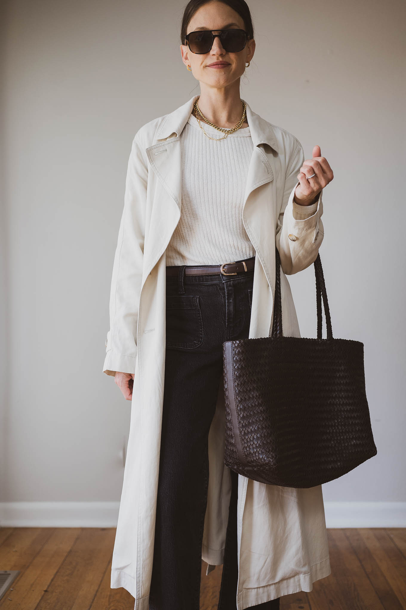 fall capsule wardrobe outfit idea with a beige fitted sweater, beige trench coat, black jeans, brown heeled ankle boots, and a brown woven tote bag