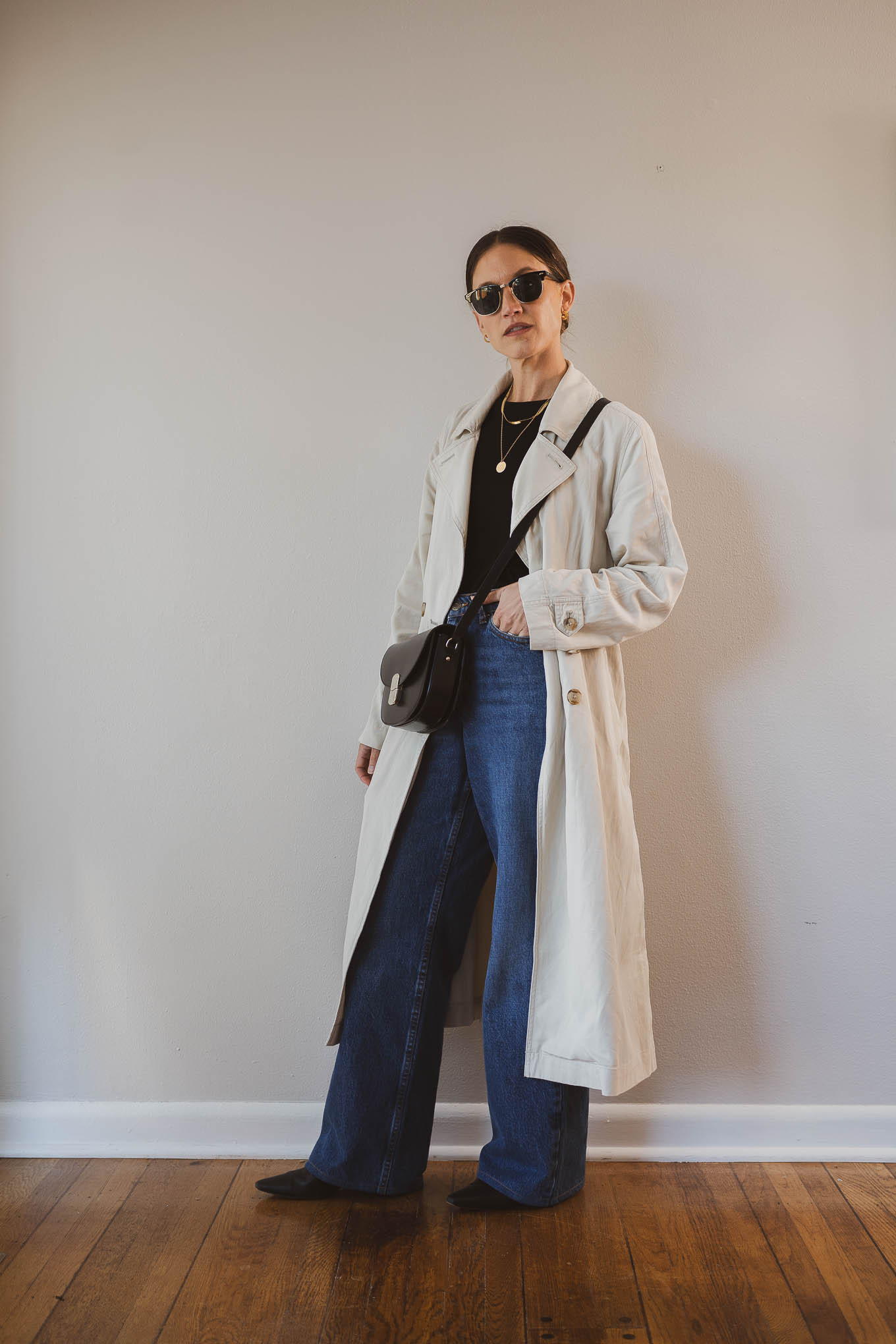 fall outfit idea with a black tee, beige trench coat, wide leg jeans, black boots, and a black crossbody bag