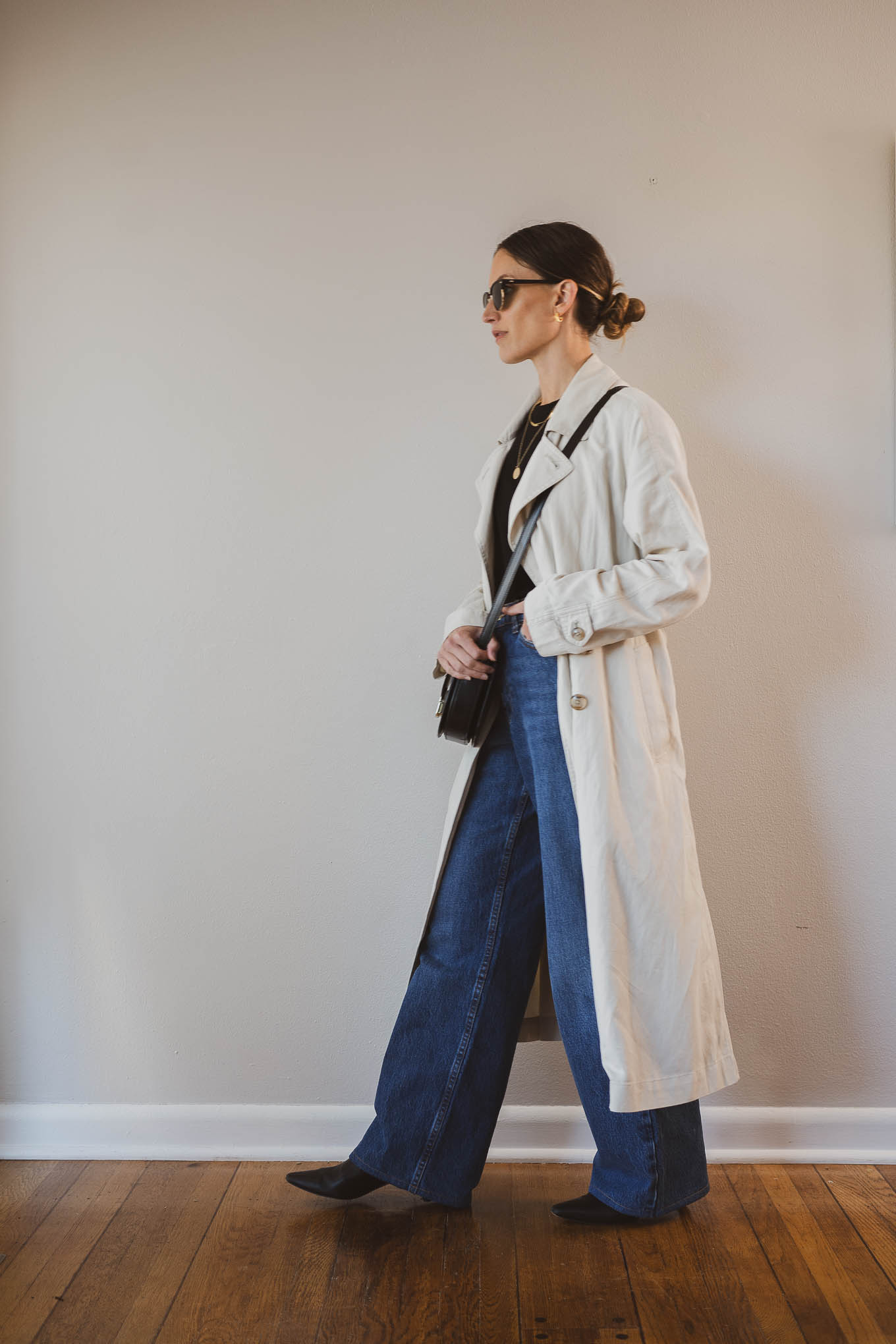 fall outfit idea with a black tee, beige trench coat, wide leg jeans, black boots, and a black crossbody bag