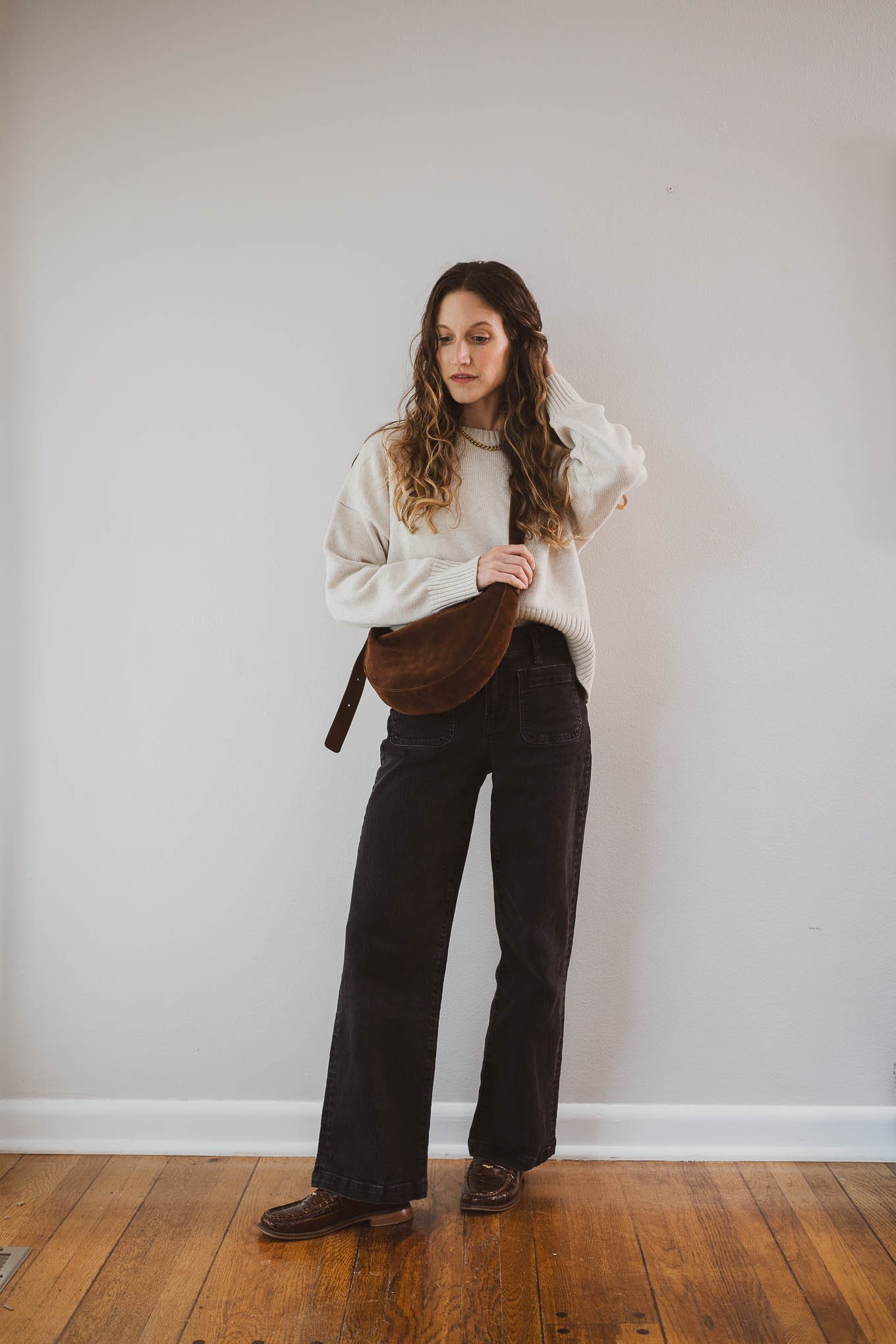 fall outfit idea with a cream sweater, black jeans, brown loafers, and a suede crossbody bag