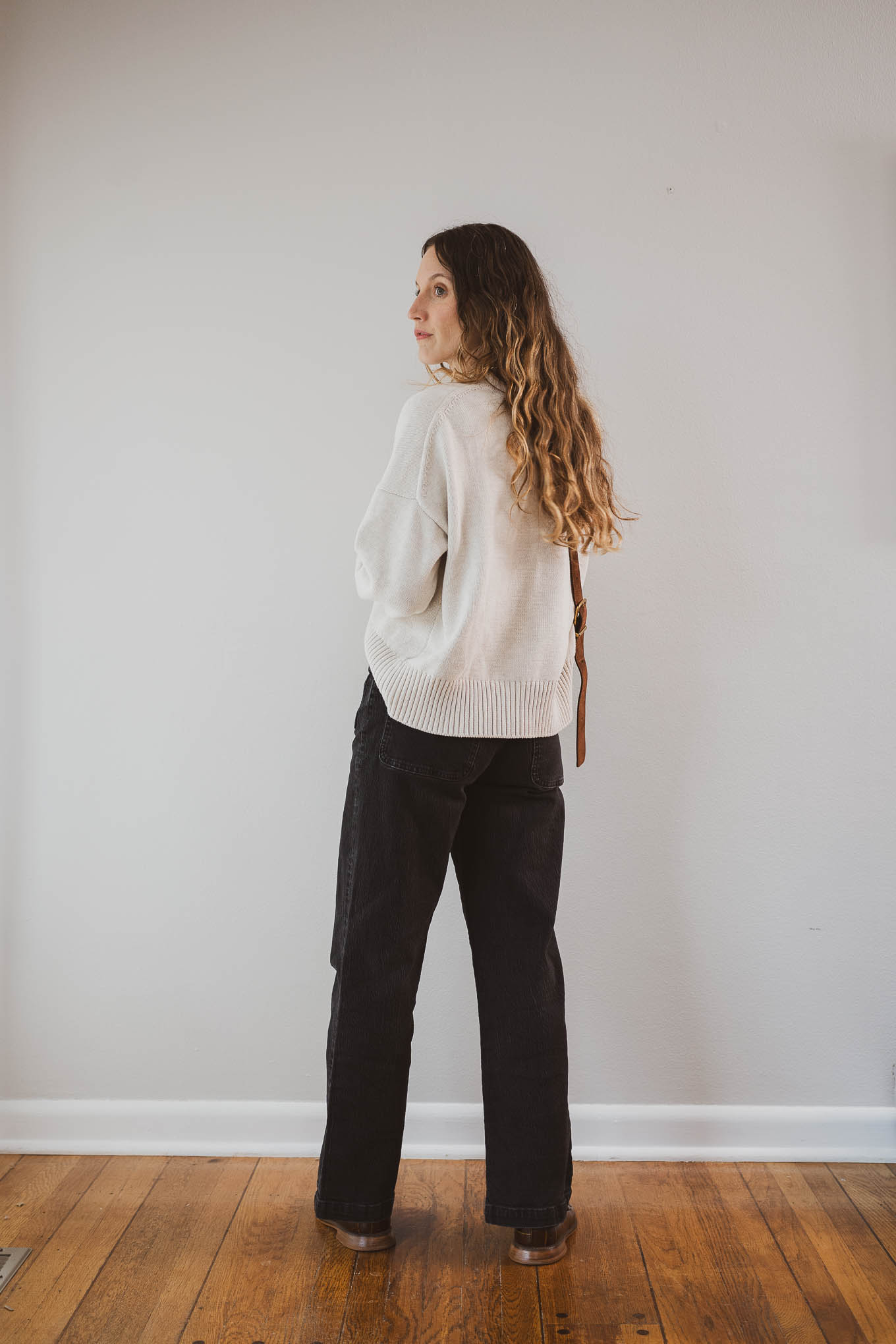 fall outfit idea with a cream sweater, black jeans, brown loafers, and a suede crossbody bag