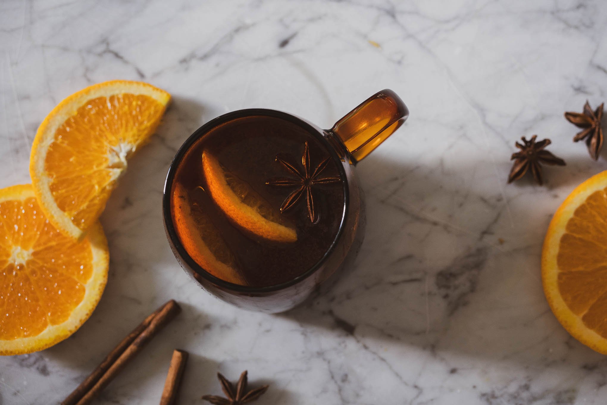a picture of non-alcoholic mulled wine; an amber glass mug with non-alcoholic mulled wine with 2 slices of oranges and a star anise pod on a marble table