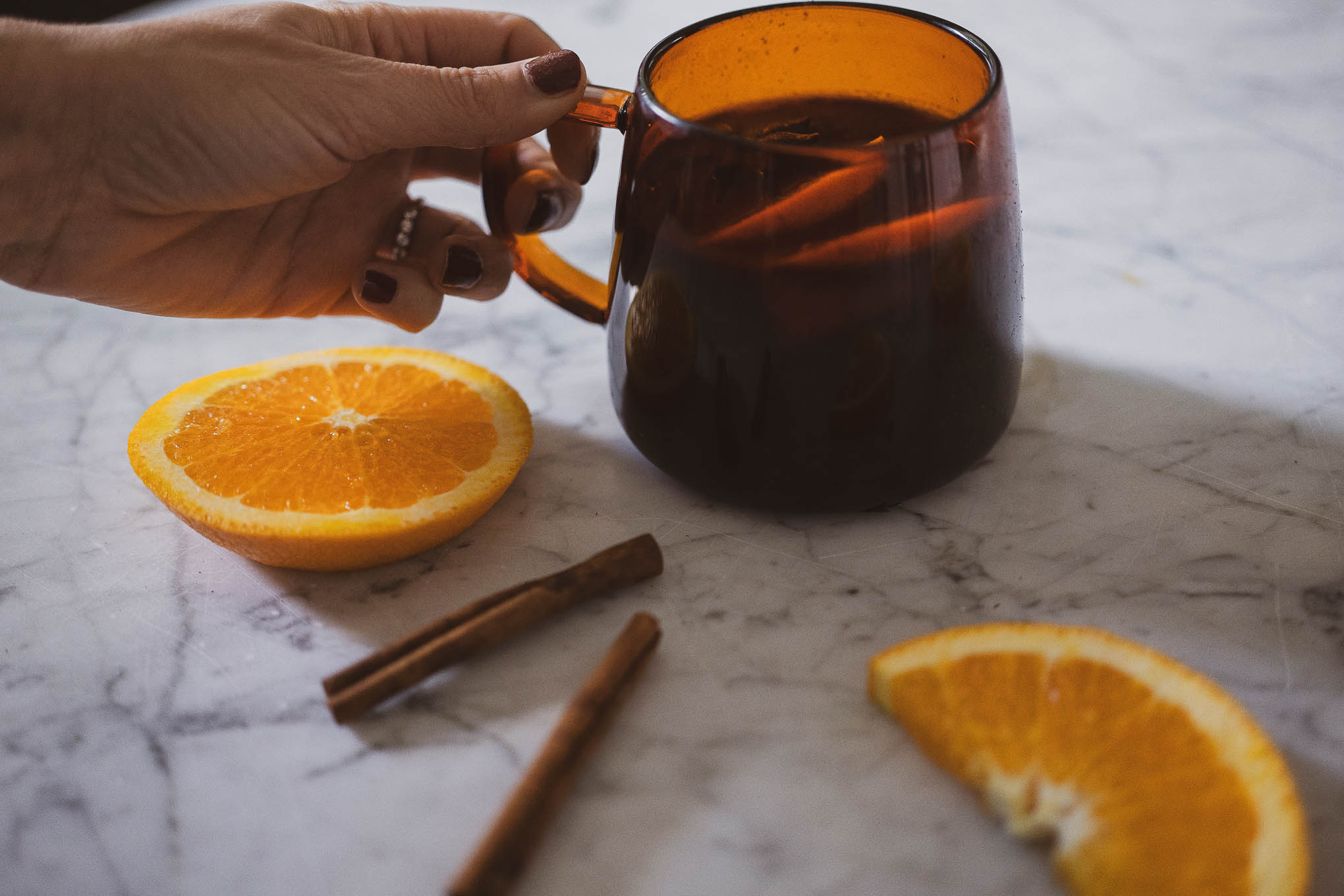 a picture of non-alcoholic mulled wine; an amber glass mug with non-alcoholic mulled wine with 2 slices of oranges and a star anise pod on a marble table