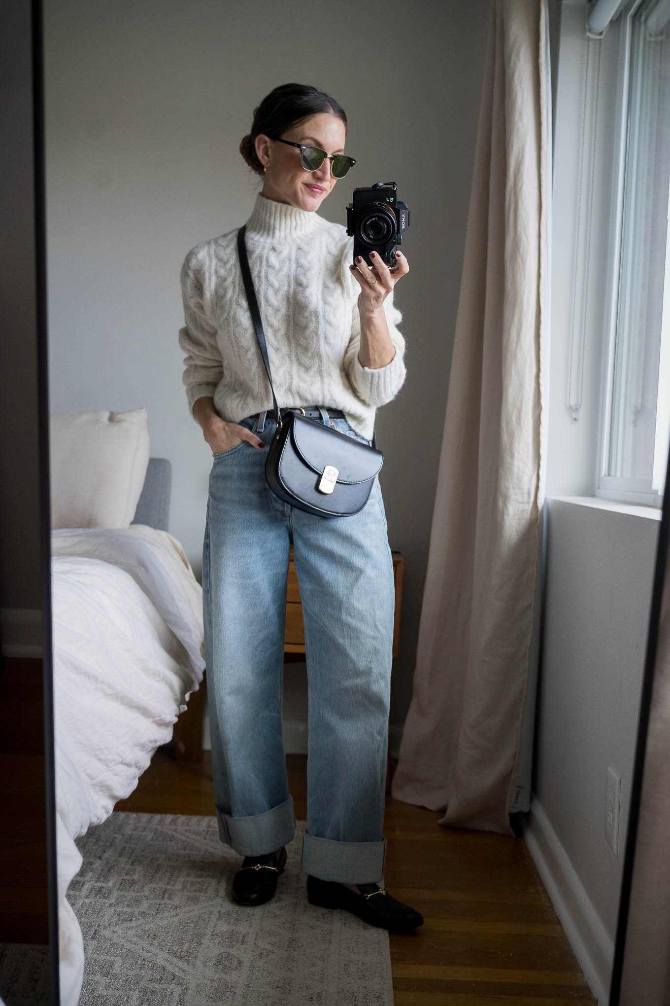 casual winter outfit with a cream cable knit sweater, light wash cuffed jeans, black loafers, and a black crossbody bag