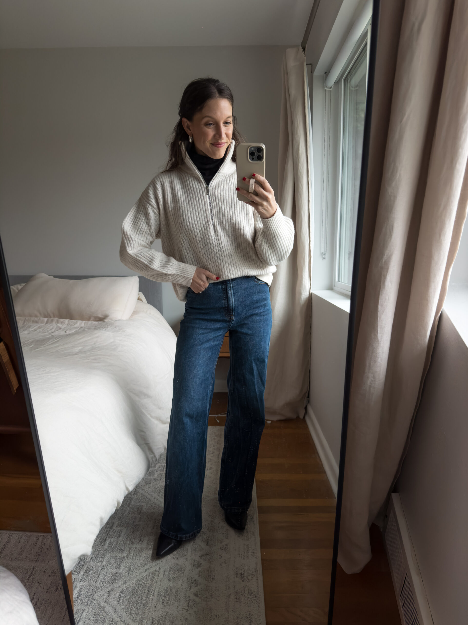 casual chic winter outfit with a black turtleneck, beige half-zip sweater, full length dark wash jeans, and black heeled boots