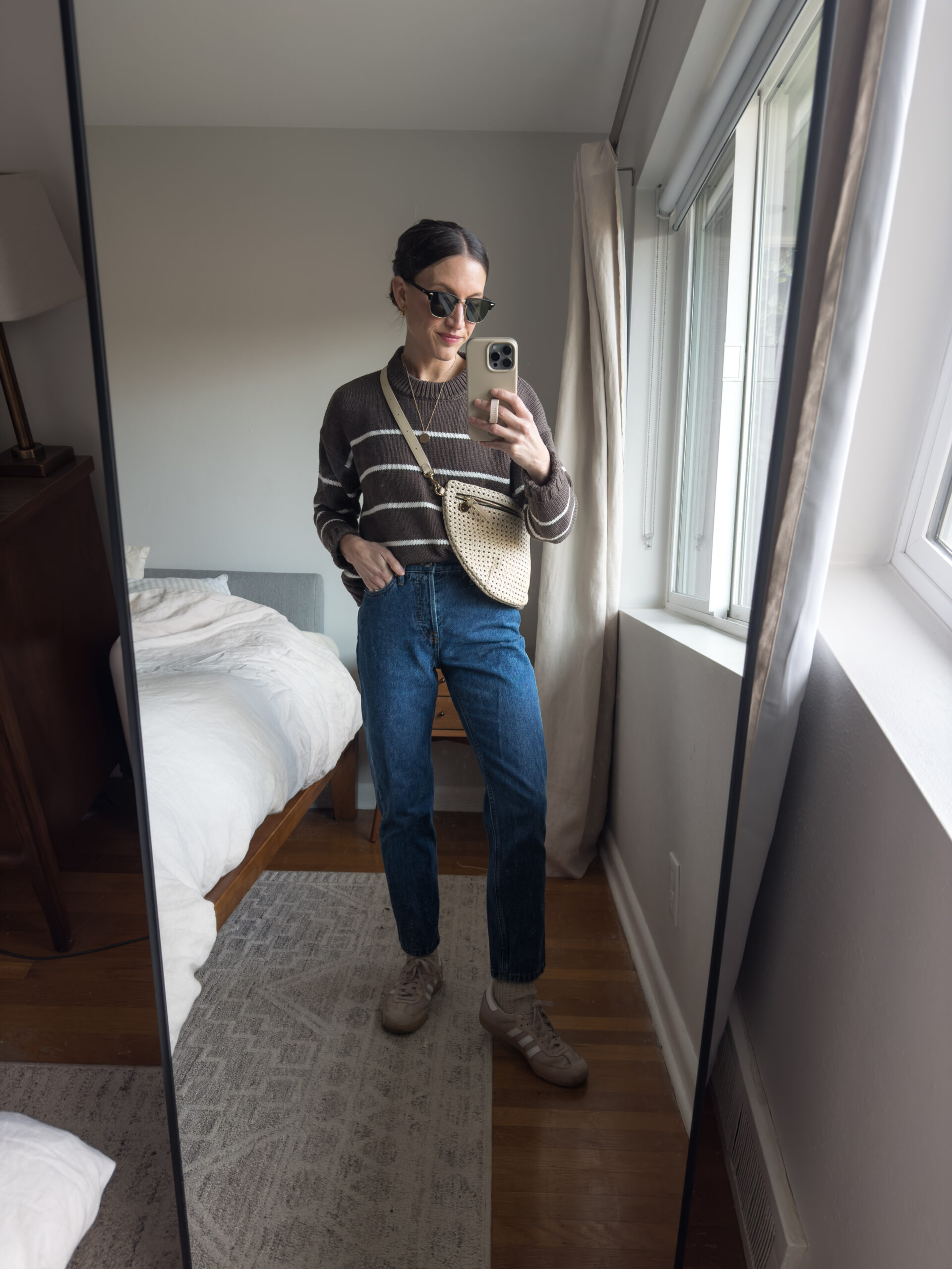 casual winter outfit with a brown and white striped sweater, slim cut jeans, tan Adidas Samba sneakers, and a cream sling bag
