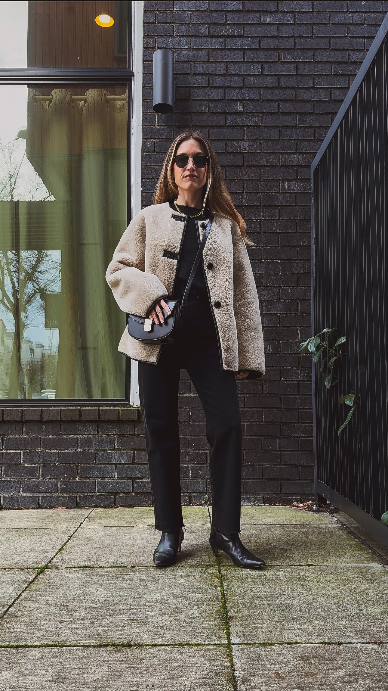 casual chic winter outfit with a black sweater, black straight leg jeans, black heeled boots, a faux fur coat, and a black crossbody bag