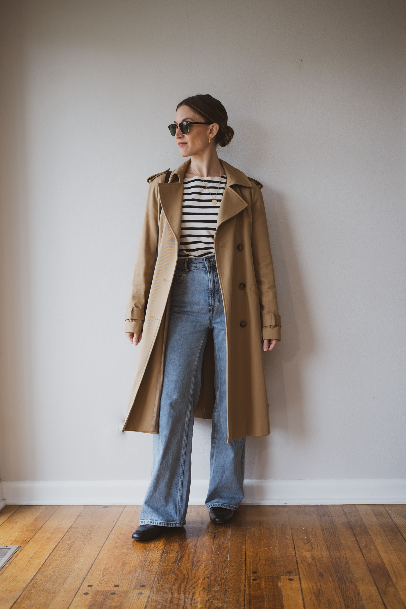 how to style loafers with a black and white striped tee, tan trench coat, light wash full length jeans, and black loafers