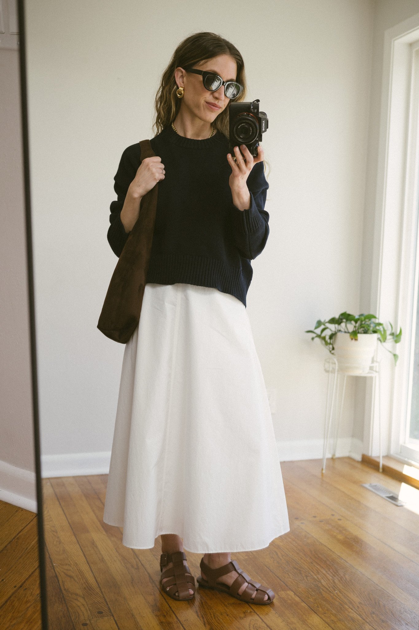 white poplin skirt outfit with a navy sweater, white skirt, brown leather fisherman sandals, and a brown suede bag