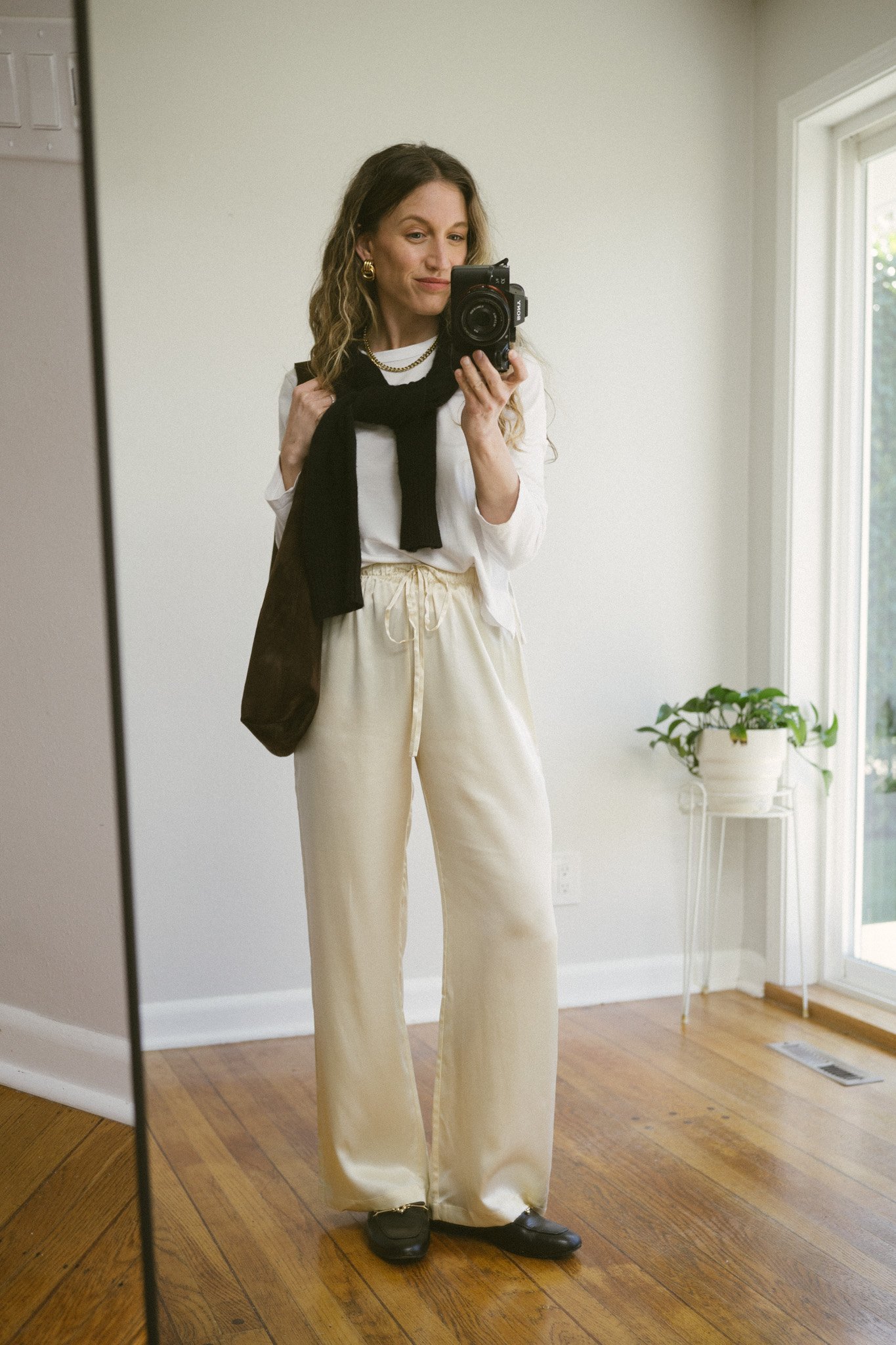 silk pant outfit with a white tee, black cashmere sweater over the shoulders, cream silk pants, and black leather loafers