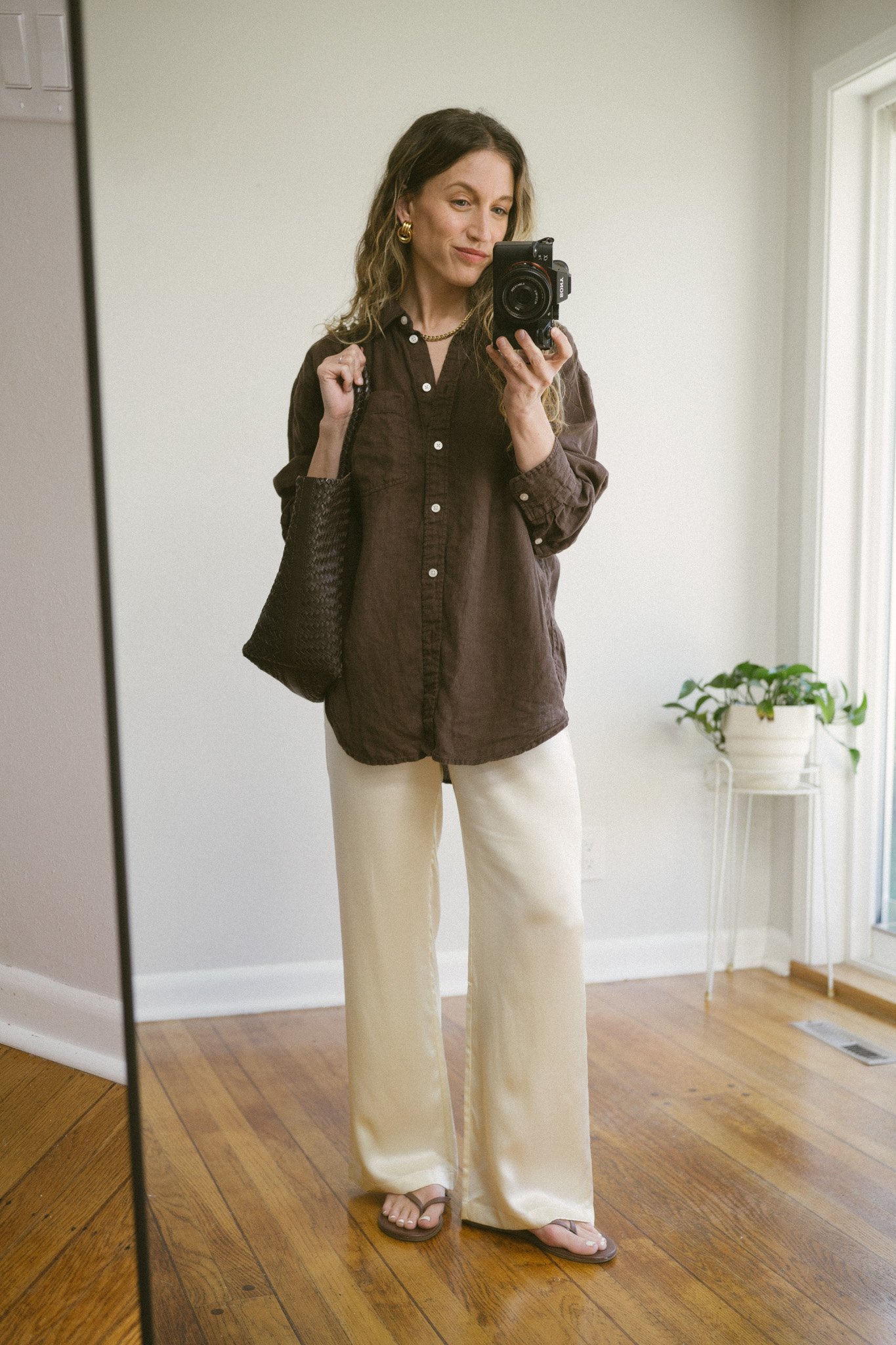 silk pant outfit with a brown linen button down shirt, cream silk pants, brown flip flops, and a brown woven bag