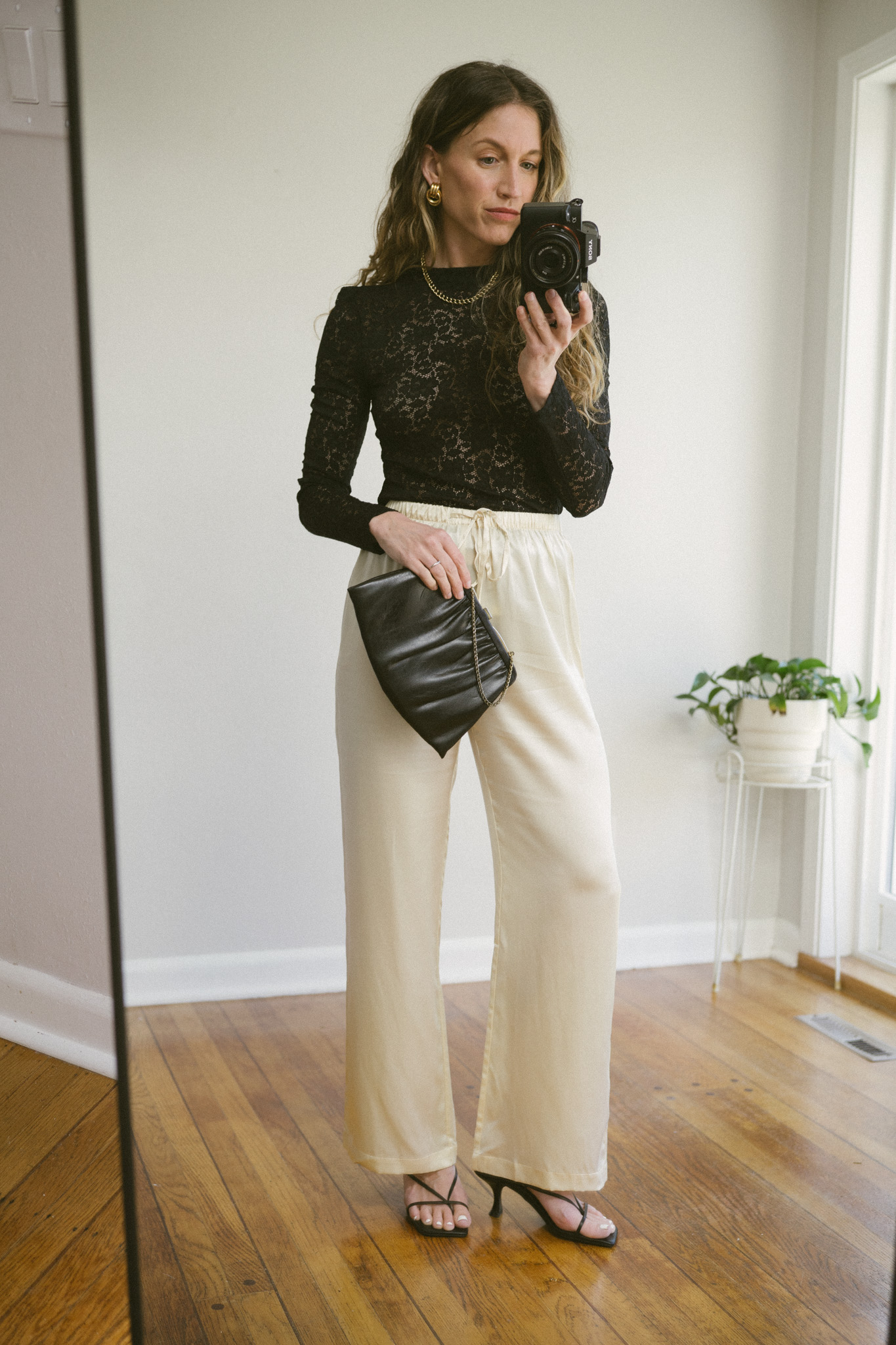 silk pants outfit with a black lace blouse, cream silk pants, black strappy heels, and a black clutch bag