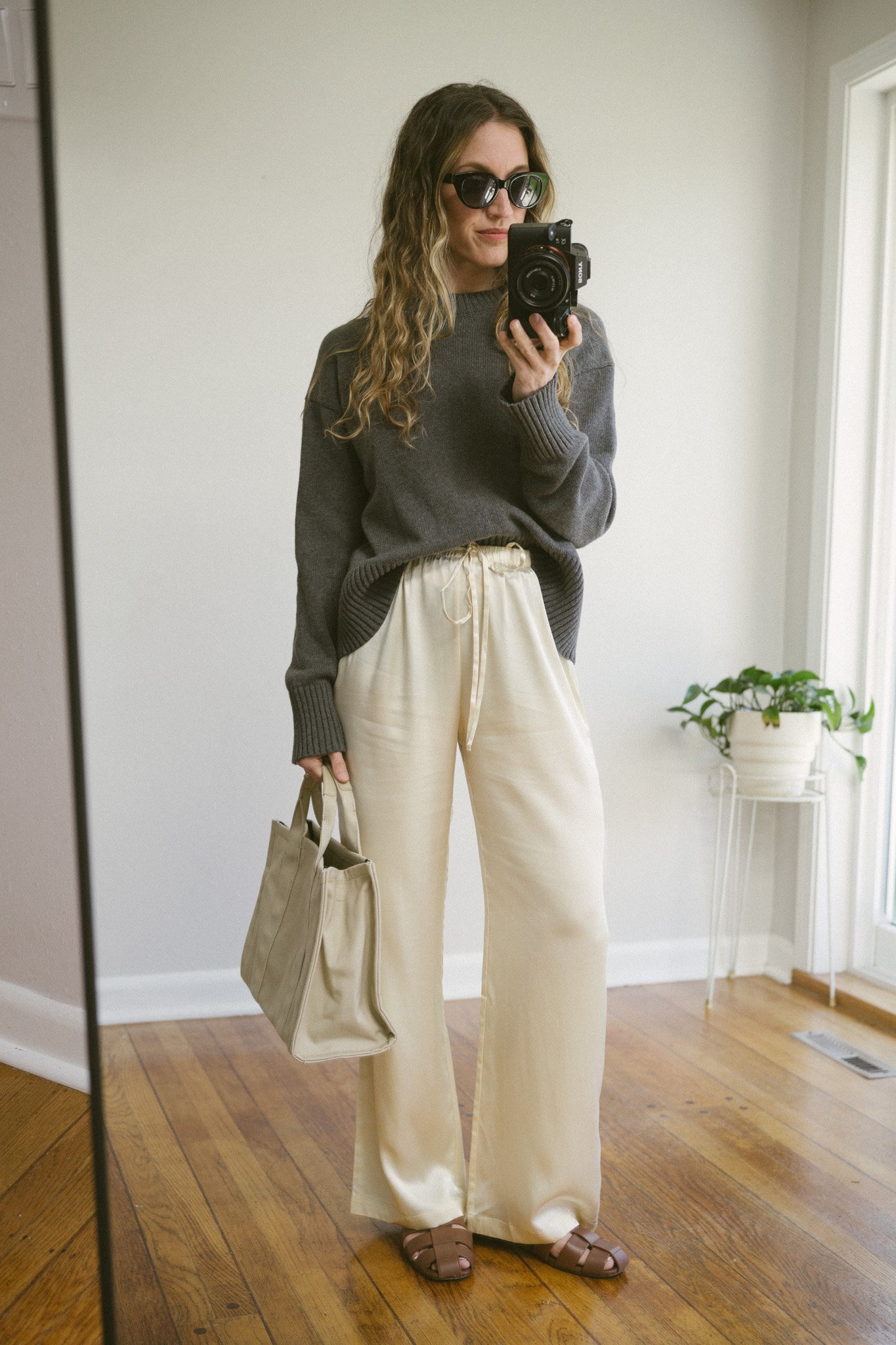 silk pants outfit idea with a gray cotton sweater, cream silk pants, brown leather fisherman sandals, and a beige canvas bag